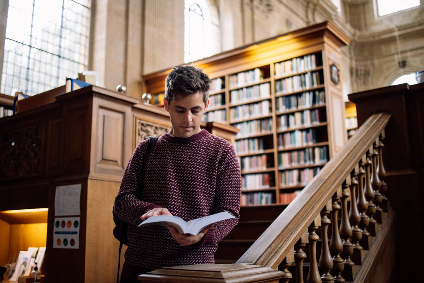 Student standing on stairs reading a book in the library