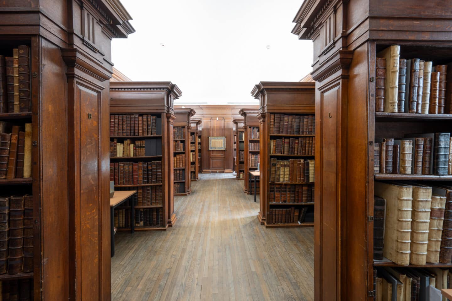 Rows of tall wooden bookcases filled with early printed and rare books, lining a central corridor with wooden flooring.