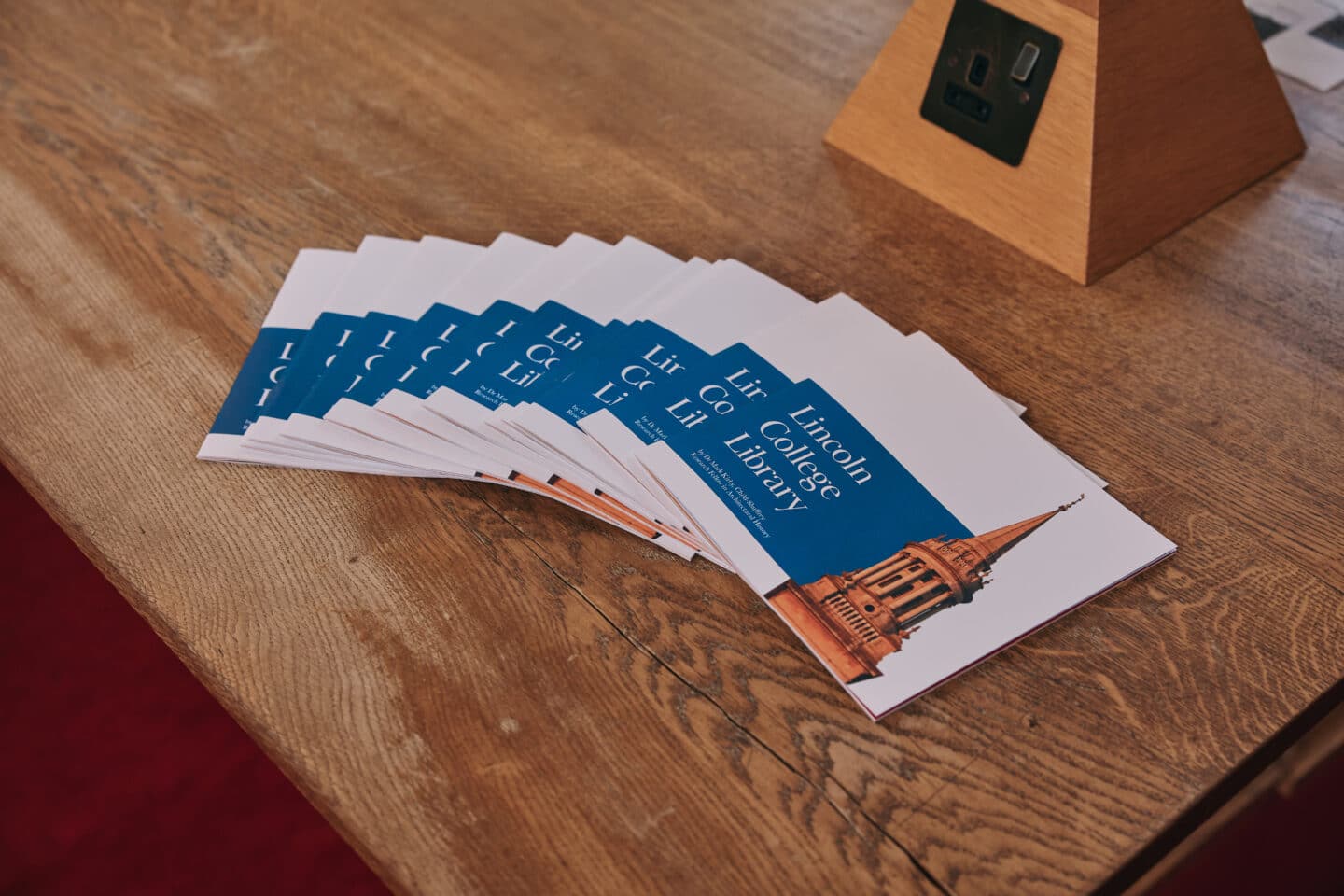 A row of Lincoln College Library brochures neatly arranged on a wooden table, featuring a blue and white design with an image of the library on the cover