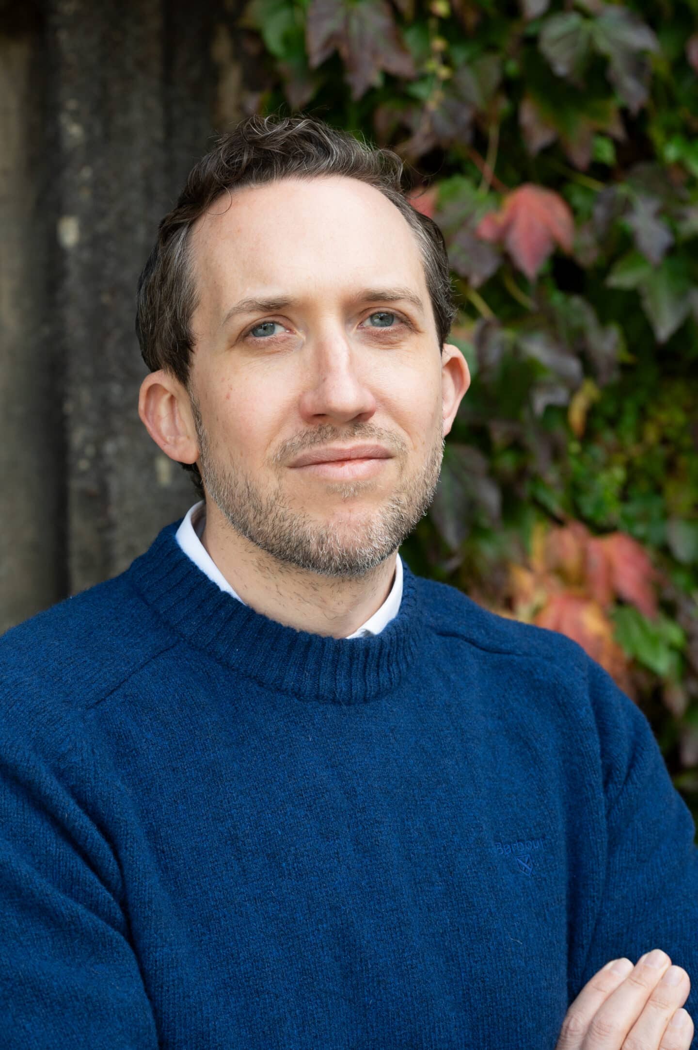 Alexander Prescott-Couch standing in Front Quad at Lincoln College, Oxford, with green and red ivy leaves behind.