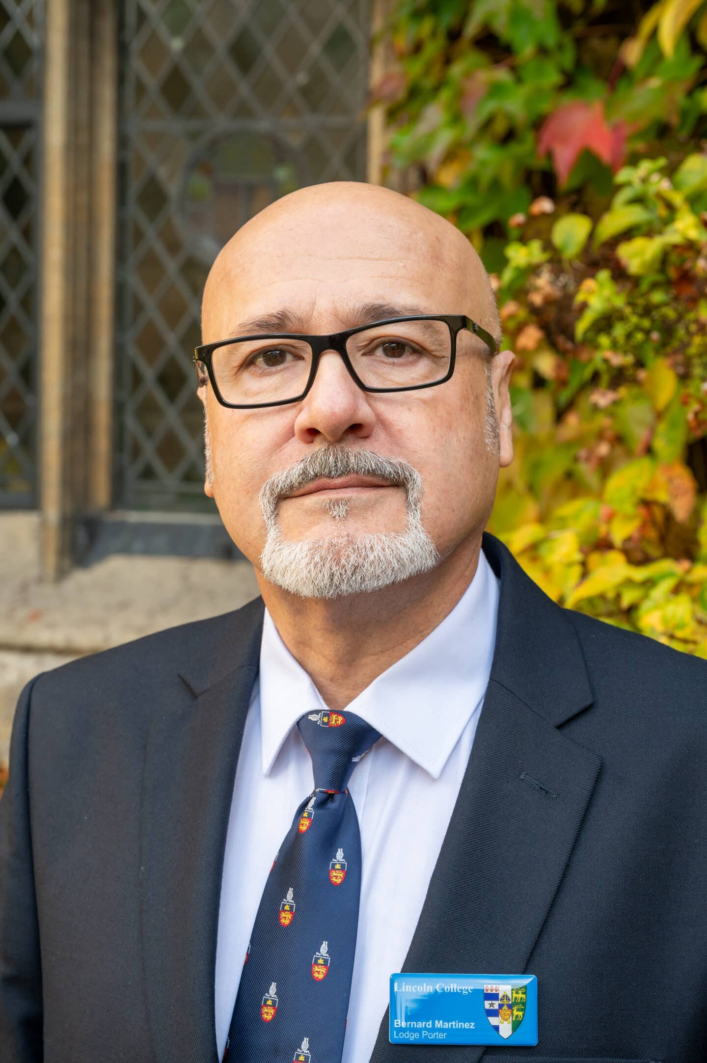 Bernard Martinez standing in Front Quad at Lincoln College, Oxford, wearing a suit and College tie, with ivy and stone window in the background.