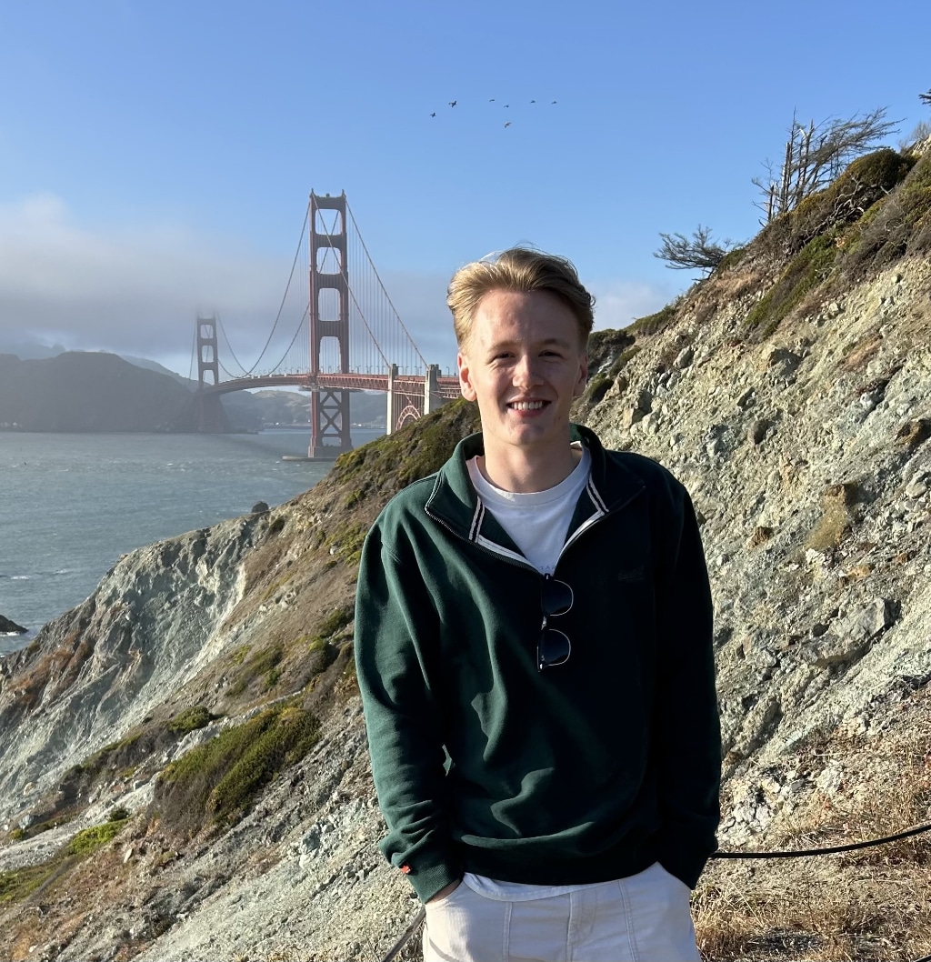 Chris Paton standing on a coastal trail overlooking the Golden Gate Bridge in San Francisco on a clear day, with low cloud around the bridge and ocean in the background