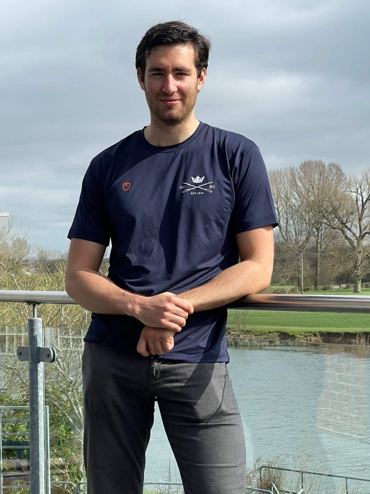 A young man in a blue OUBC t-shirt with a river in the background