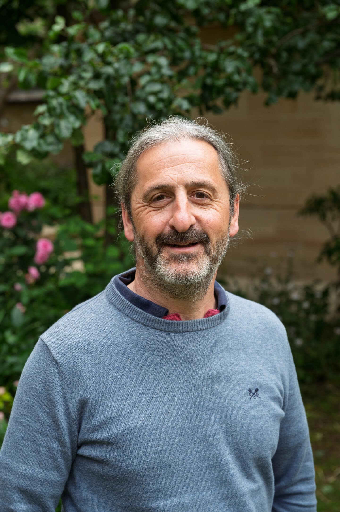 Photo of Gerard Fegan in blue jumper standing in front of green foliage with pink flowers