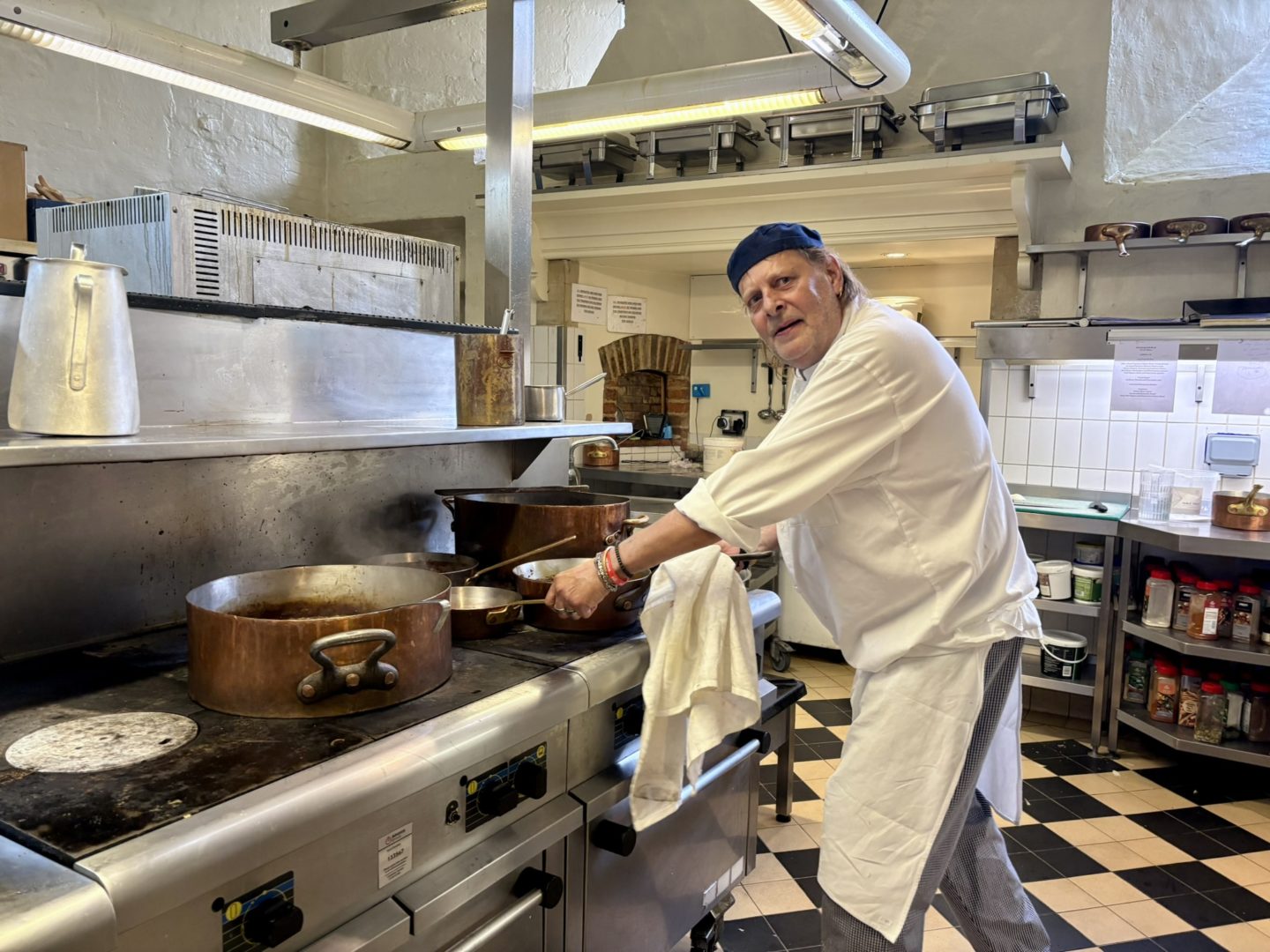 Chef in whites cooking on a gas stove with large pots