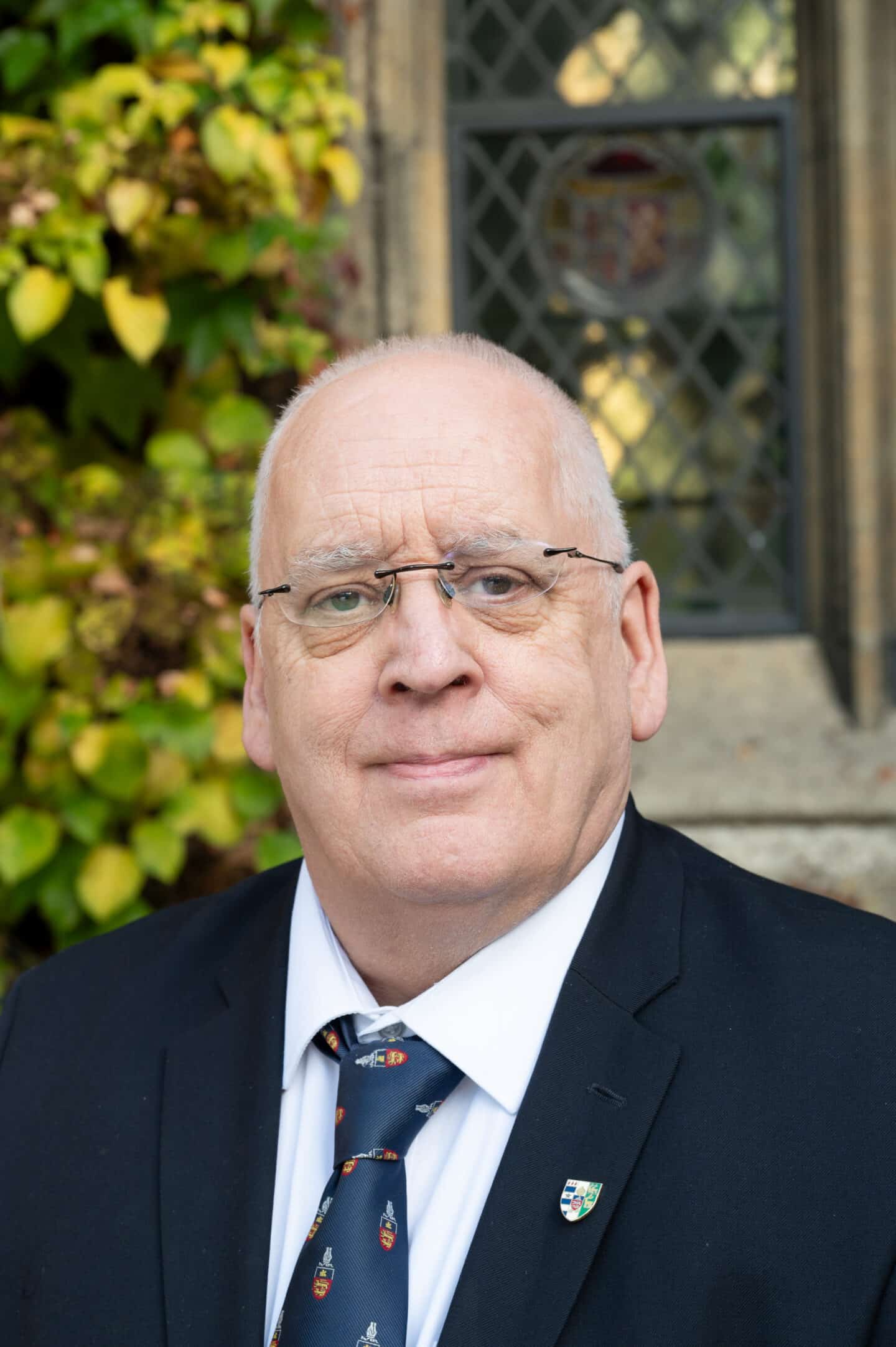 Jerry Pendleton standing in Front Quad at Lincoln College, Oxford, in a suit and College tie, with ivy and stone window behind.