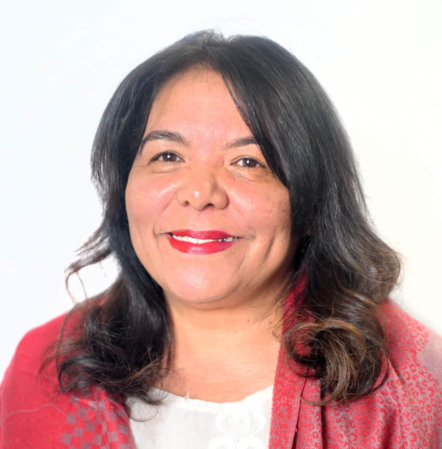 Portrait of Professor June Bam smiling at the camera, wearing a white top and red patterned shawl against a light background