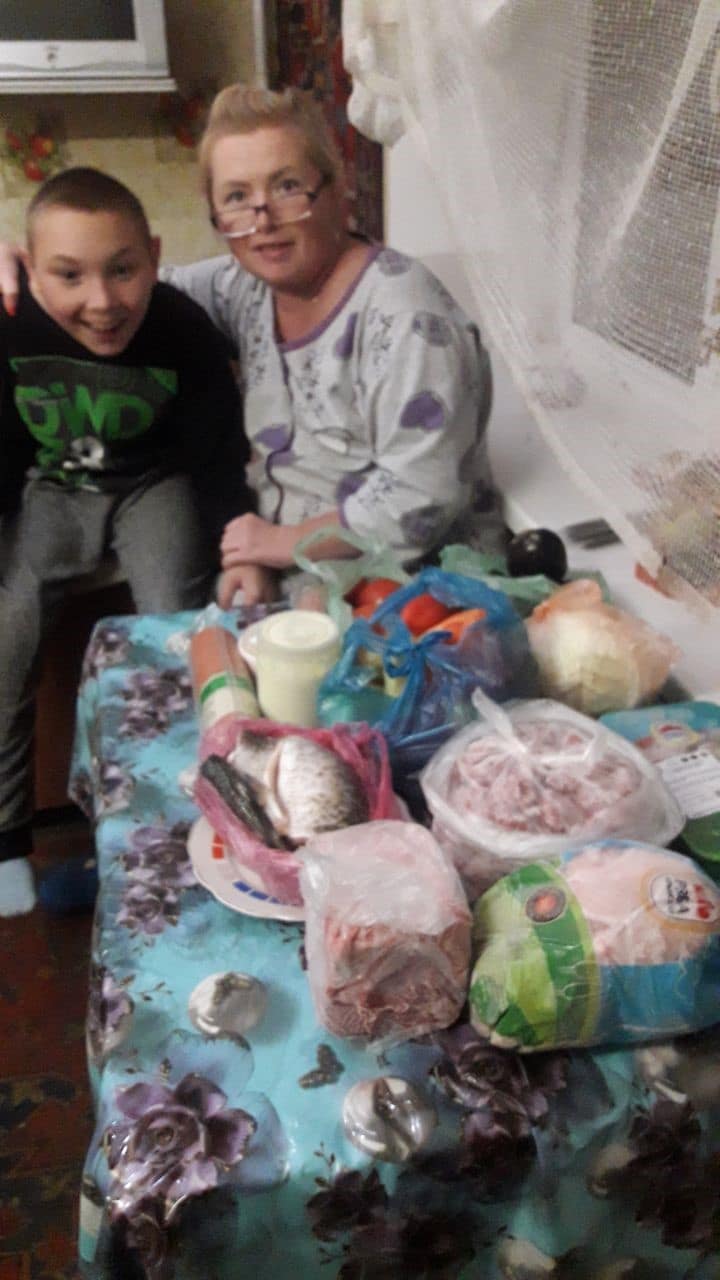 A smiling woman and young boy with a pile of groceries on the table in front of them.