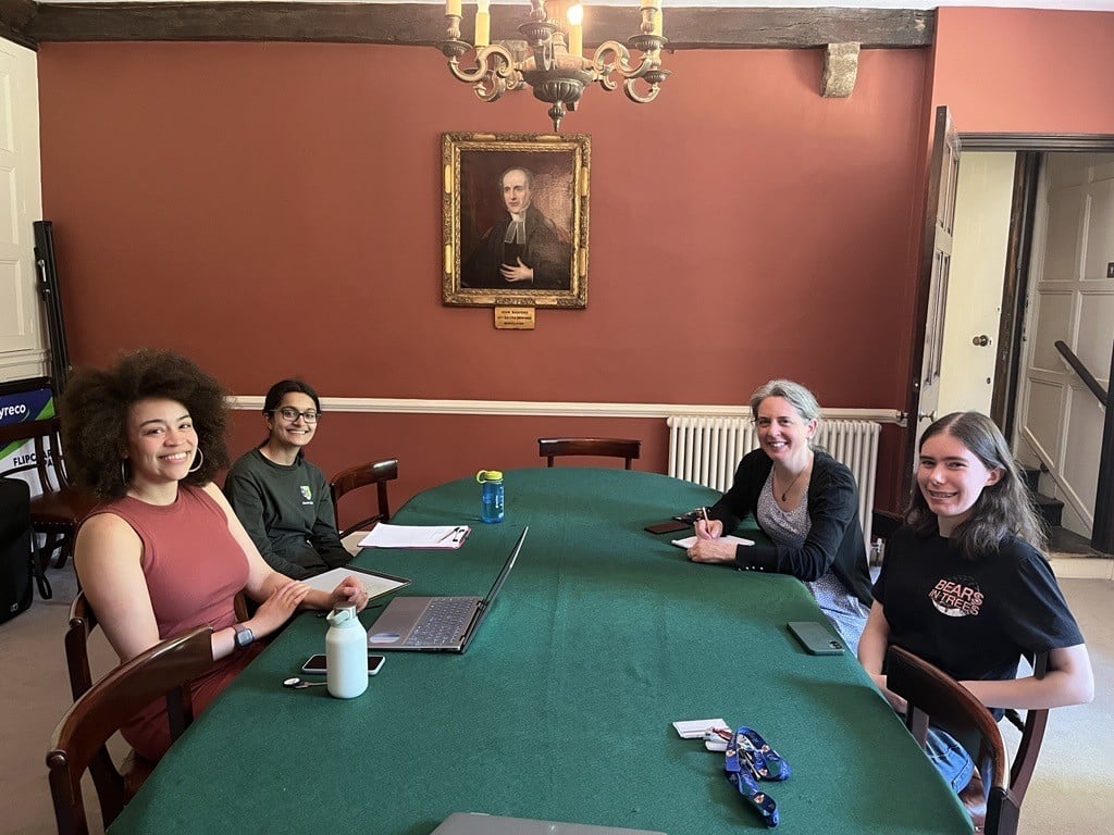 Members of Lincoln College’s Green Impact Team . Four team members are meeting and are seated around a green table, smiling towards the camera.