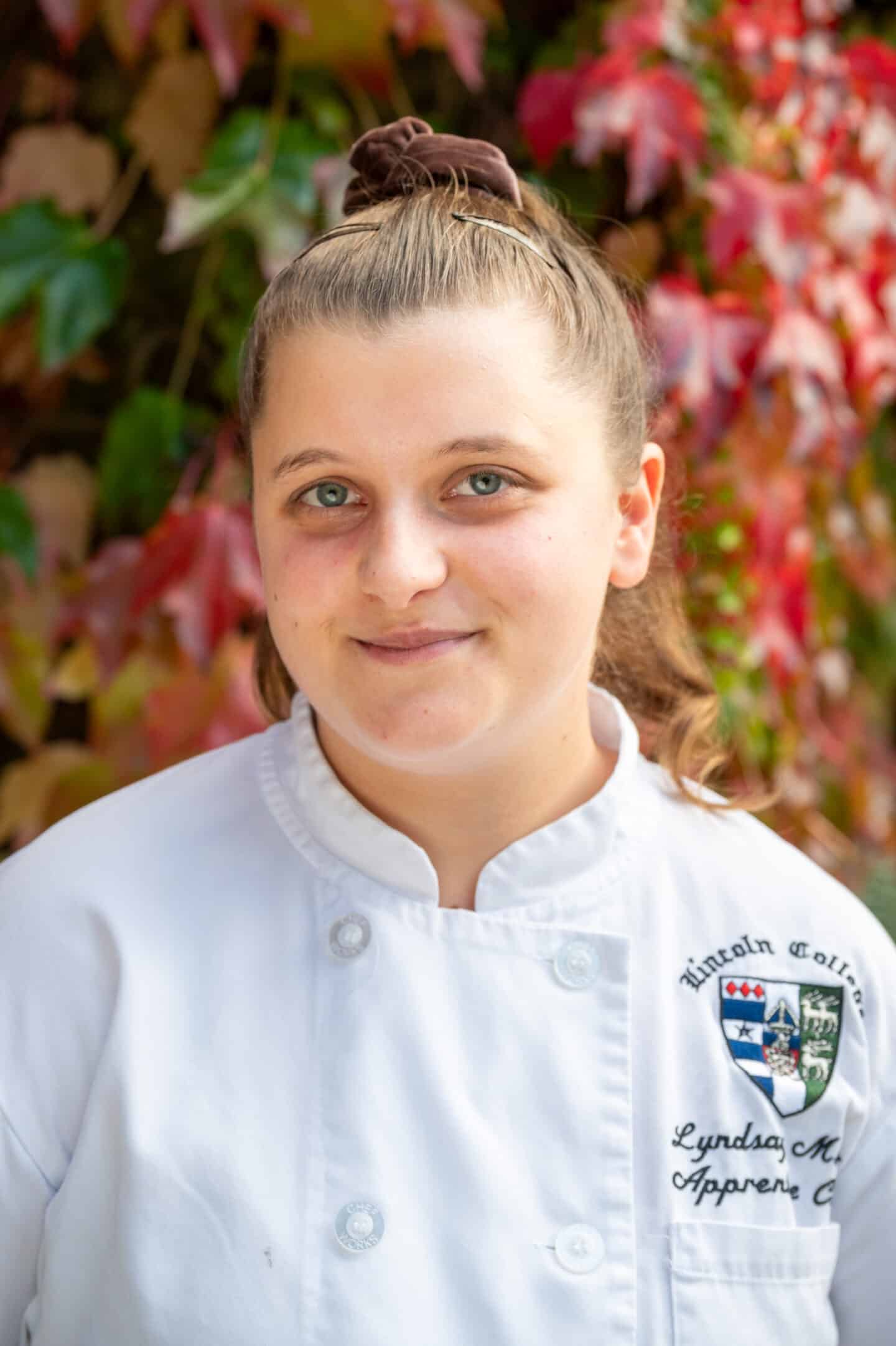 Lyndsay Marsh standing in Front Quad at Lincoln College, Oxford, wearing a white chef’s jacket with the College crest embroidered on it.