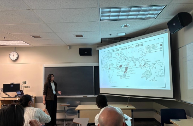 Maria Murad presenting beside a projected map titled “The British Colonial Empire”, speaking to seated students during an academic presentation.