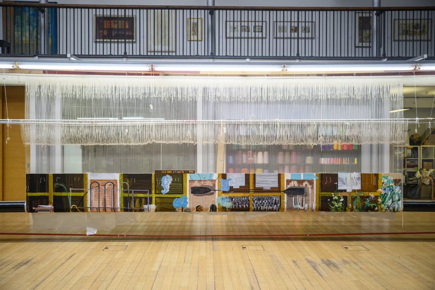 The full tapestry still on the loom in a large room with wooden floor