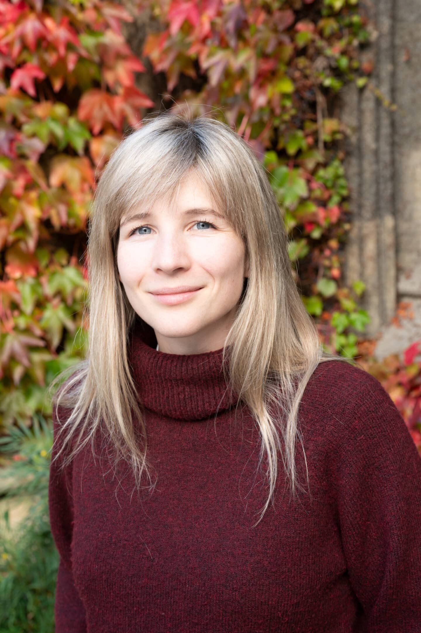 Rebecca Menmuir standing in Front Quad at Lincoln College, Oxford, wearing a burgundy jumper, with autumnal ivy in the background.