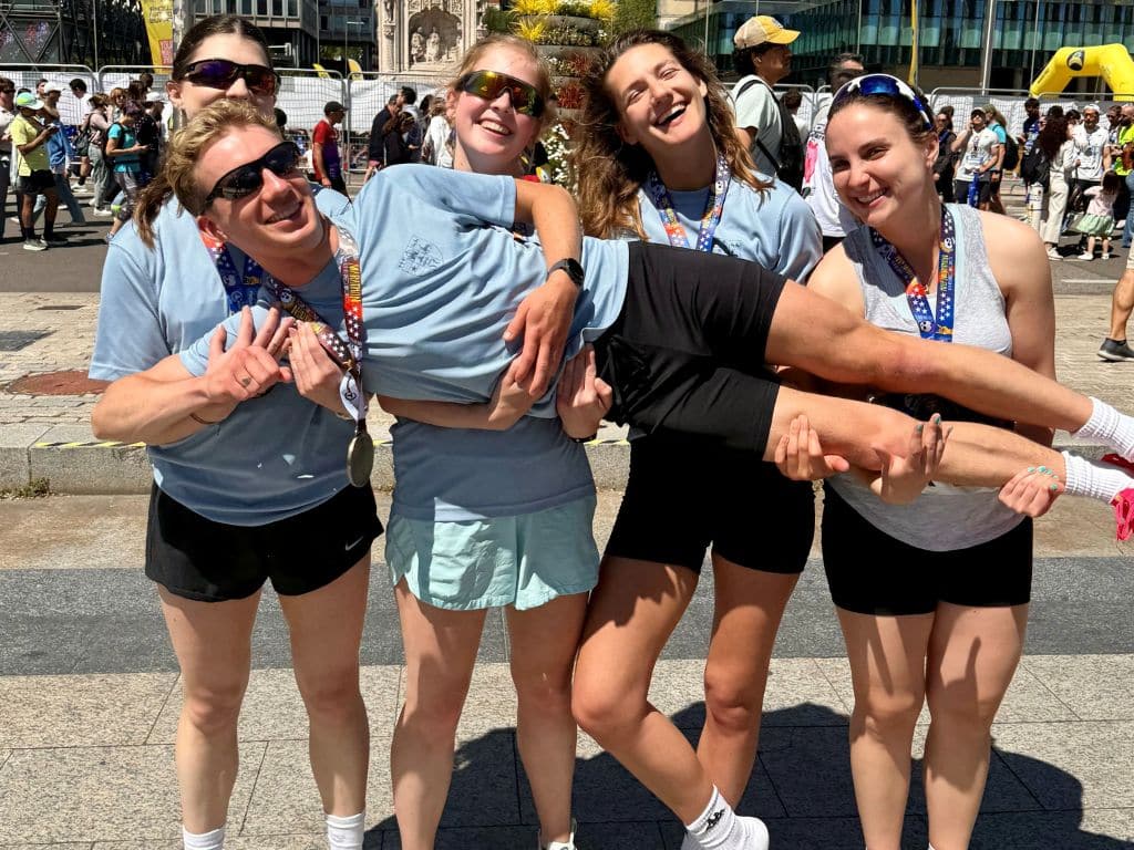 Five smiling Lincoln College students wearing medals after completing the Madrid Half Marathon, holding up teammate Peter Rory Hall in celebration.