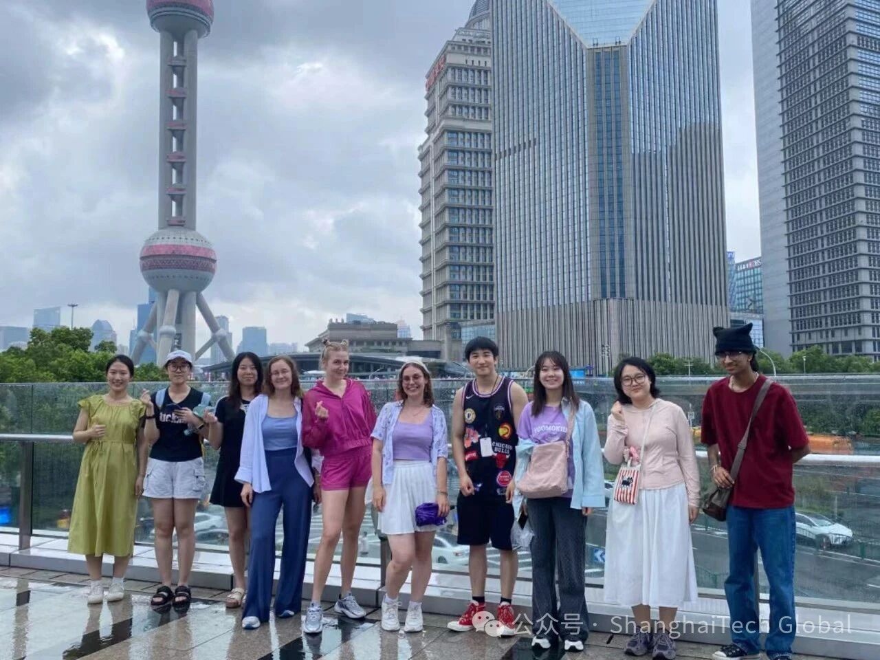Shailen Patel and fellow students posing for a group photo on a rainy day in Shanghai, with the Oriental Pearl Tower and city skyline in the background.