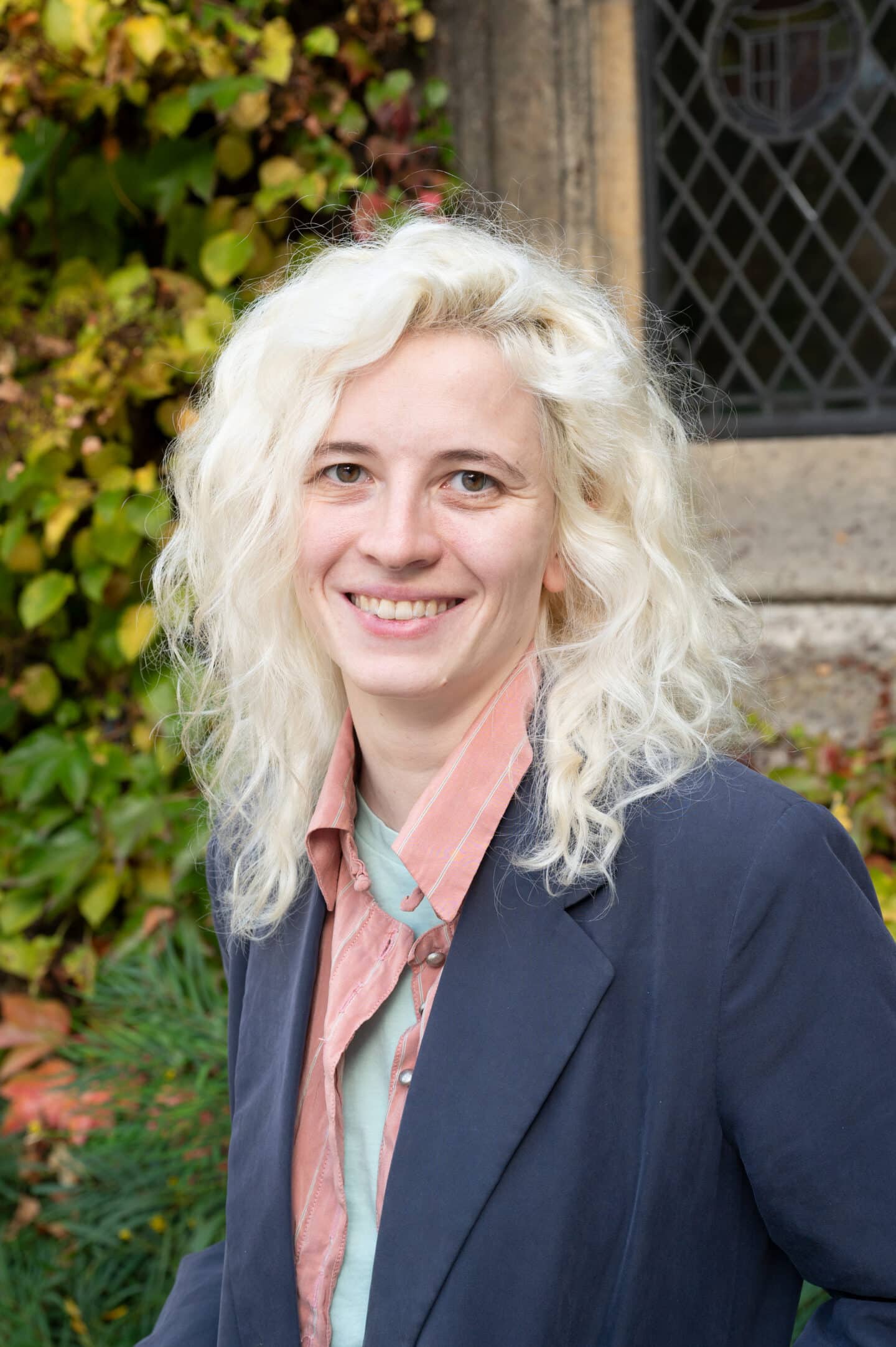 Sophia Buck standing in Front Quad at Lincoln College, Oxford, wearing a navy blazer and light pink shirt, with ivy and stonework behind.