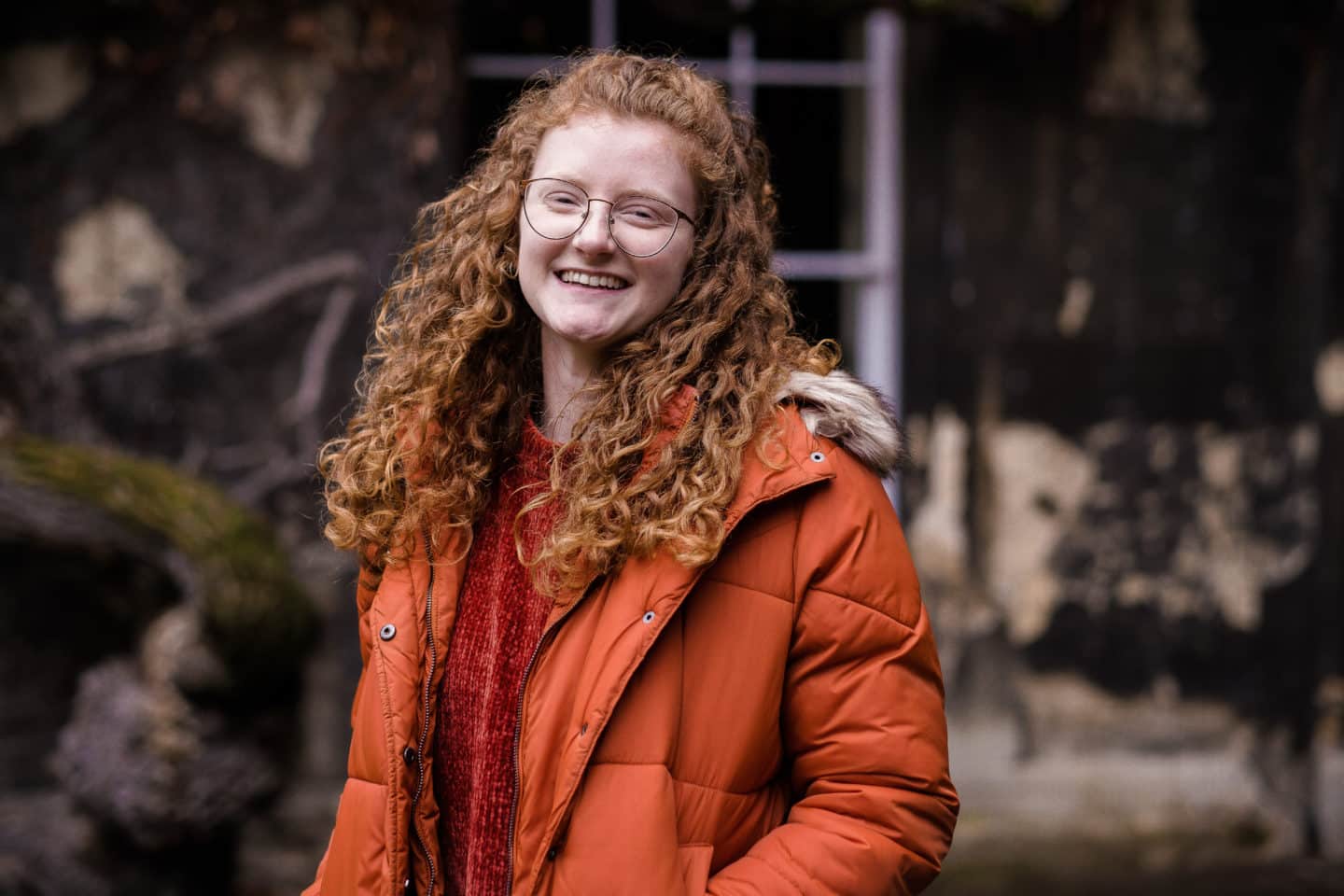 Headshot of Abigail Merchant, a young woman in glasses and an orange puffer coat