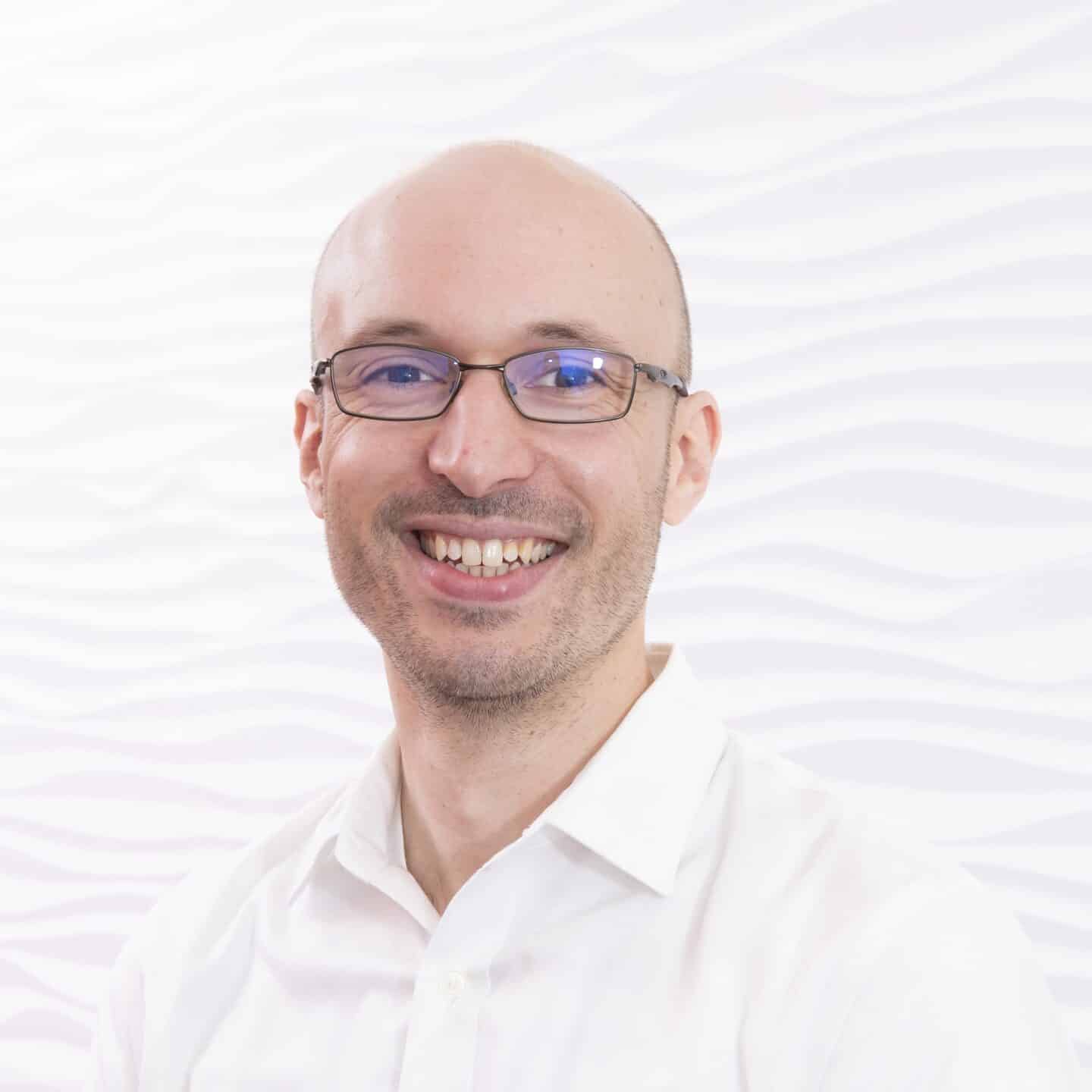 Headshot of Adam Wilkinson, a smiling man in a whites shirt and glasses
