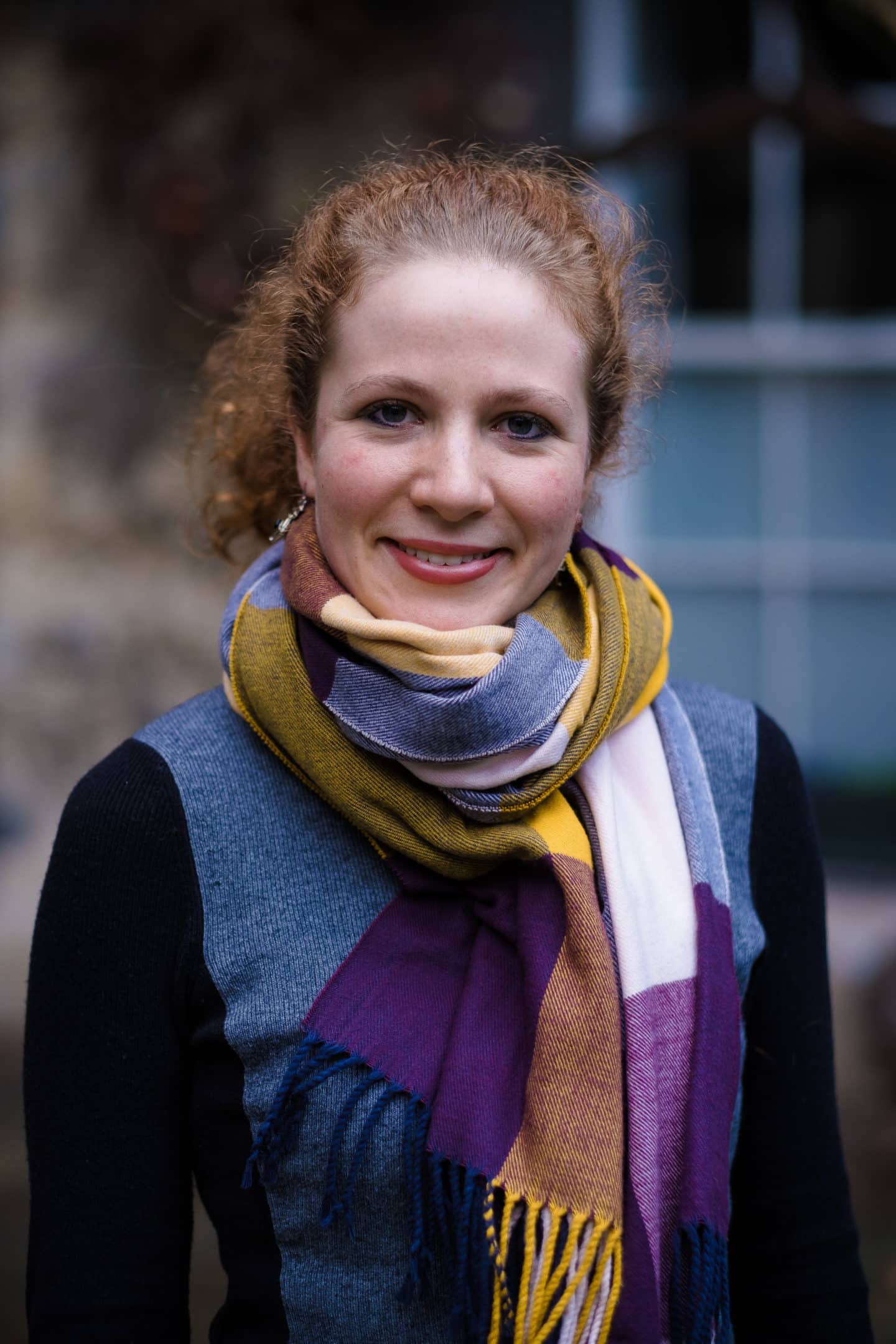 Headshot of Alexandra Brown, a young woman wearing a blue and black sweater and a colourful scarf