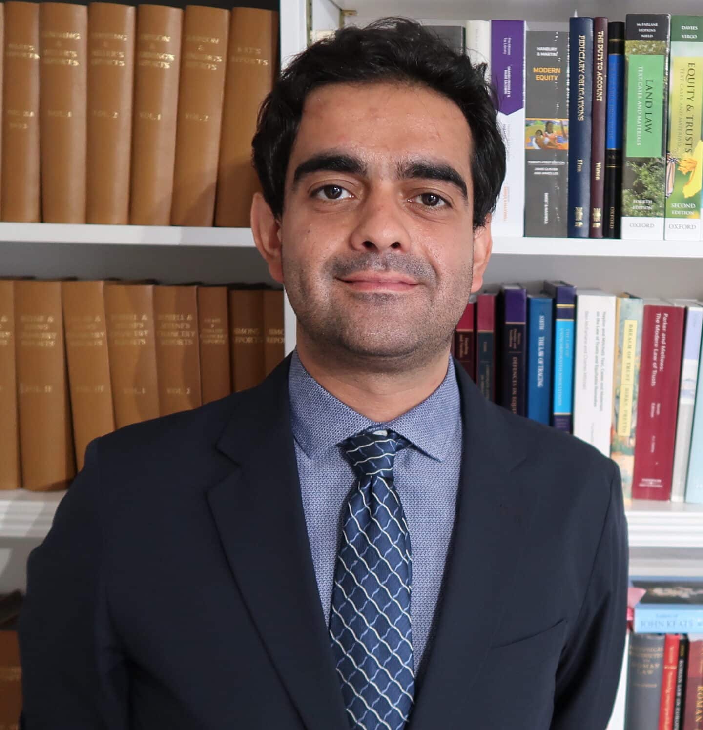 Headshot of Andreas Televantos, a man in a suit and tie in front of a bookcase.