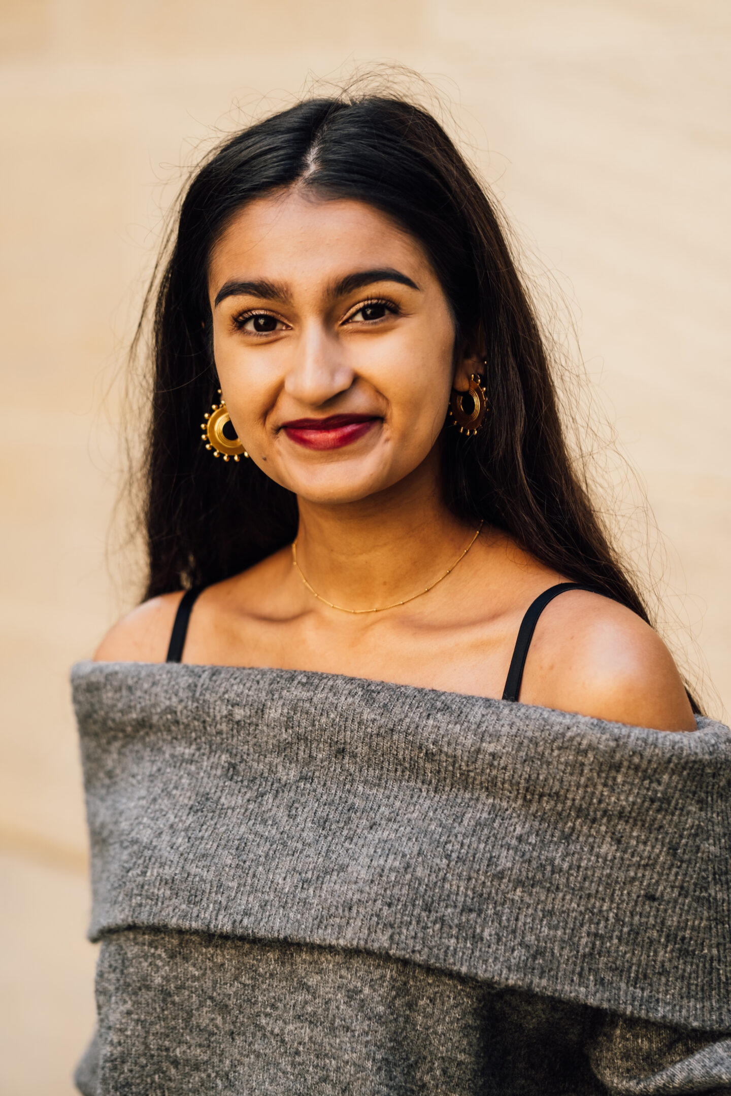 Headshot of Arya Raval, a young woman with a grey top and golden earrings