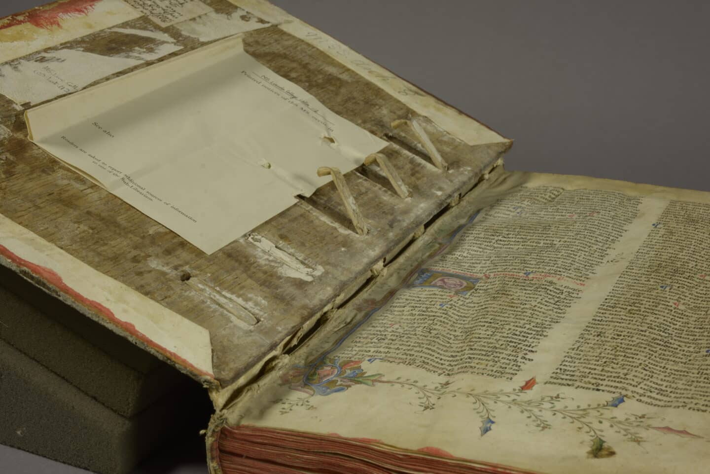 Large 15th century manuscript open to the inside cover and beautifully illustrated first page. Three support slips laced into the upper board have worked free of their lacing exit holes, and in two cases, the wooden pegs which secure the slips are missing