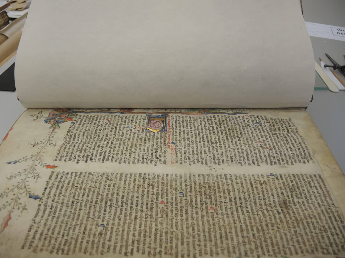 A large manuscript open to a colourfully illustrated page covered in text