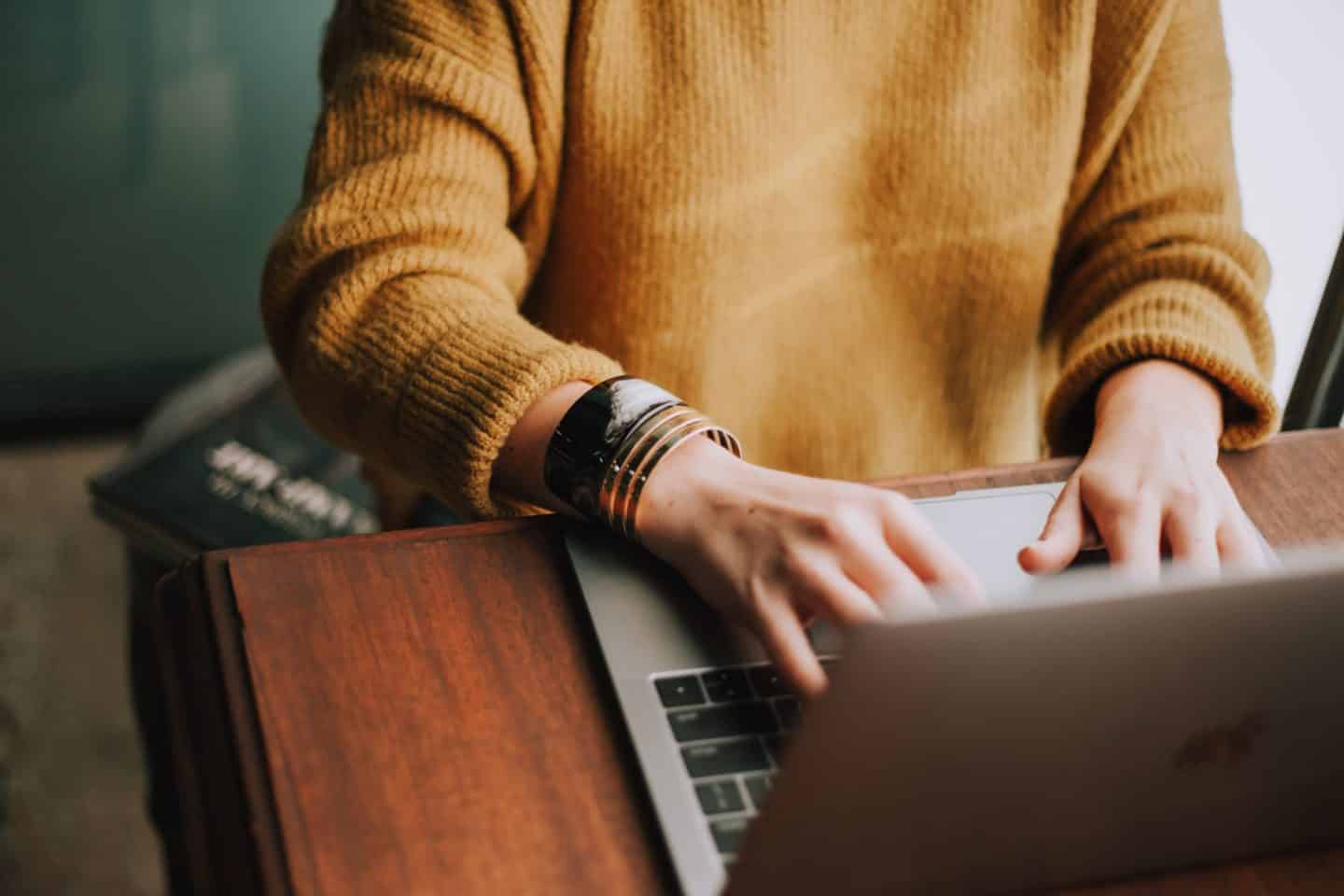 Someone in a yellow sweater typing at a laptop