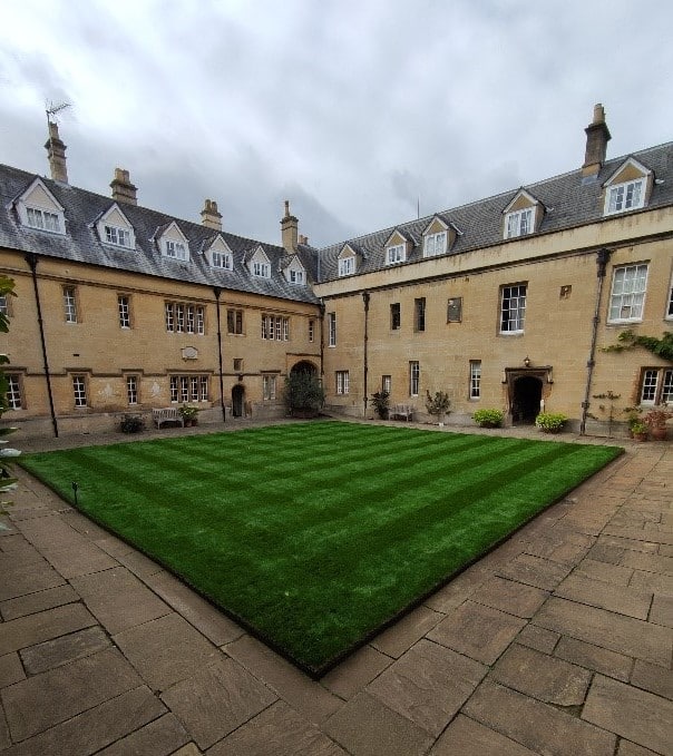 A beautifully bright green mowed lawn in the centre of a quad, with old buildings in the background.