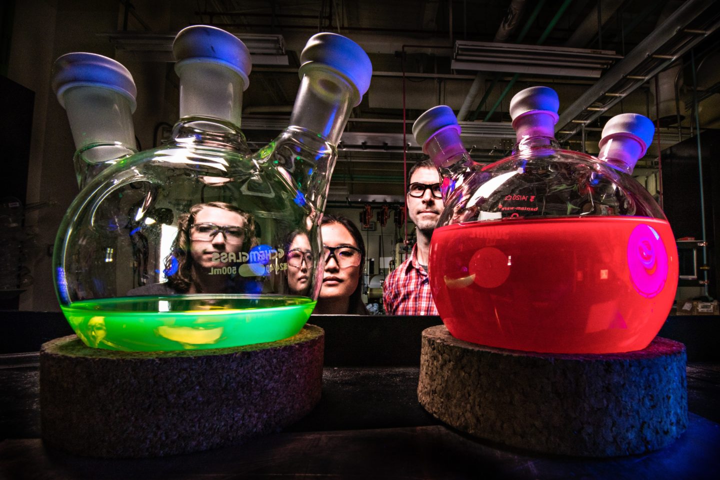 People looking at two flasks filled with green and red liquids