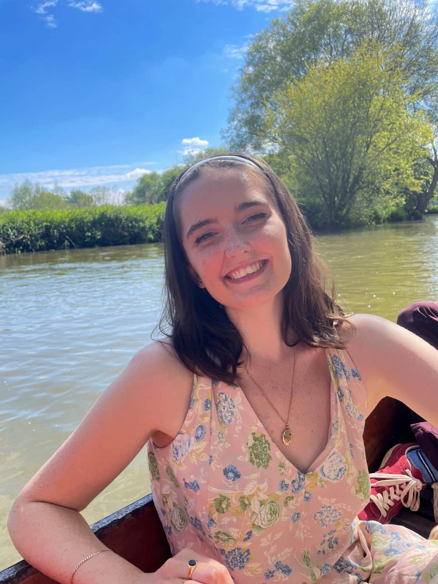 Headshot of Evie Sutcliffe, a smiling young woman in a boat on a river