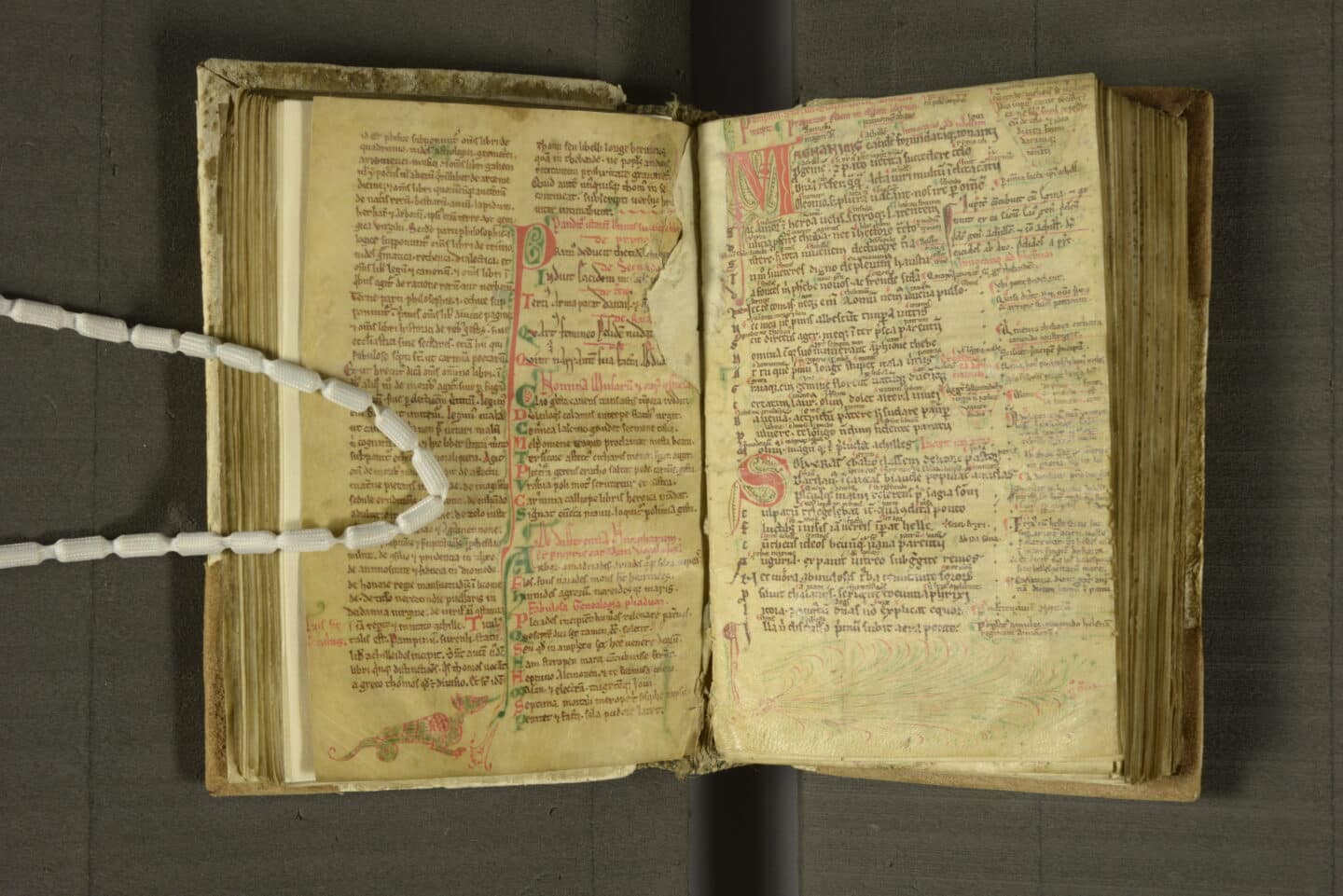 A 12th century manuscript open to pages with lots of text and some colourful illustrations and marginal inscriptions