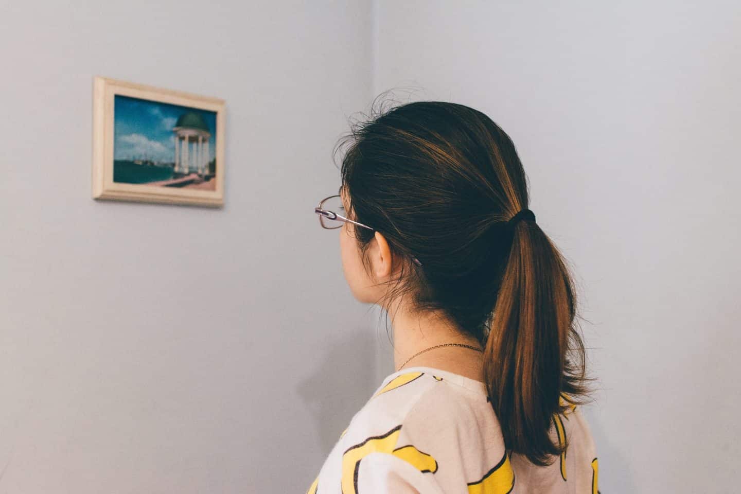 A woman in glasses looking at a small framed painting