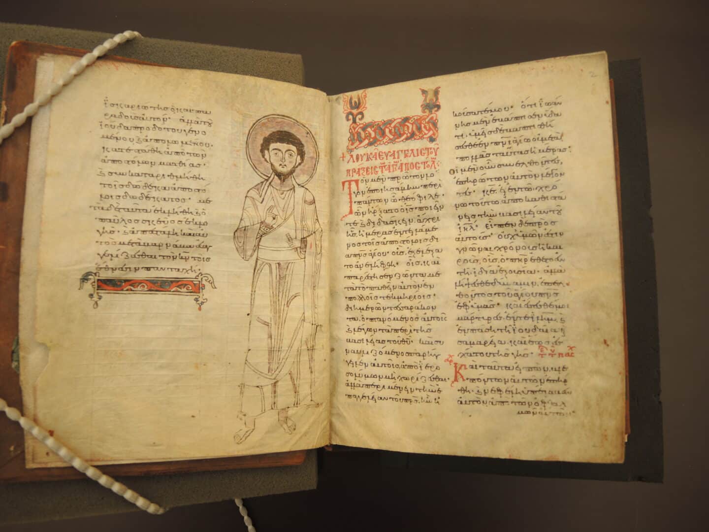 A 12th century manuscript open to pages with Greek text and a large illustration of an Apostle