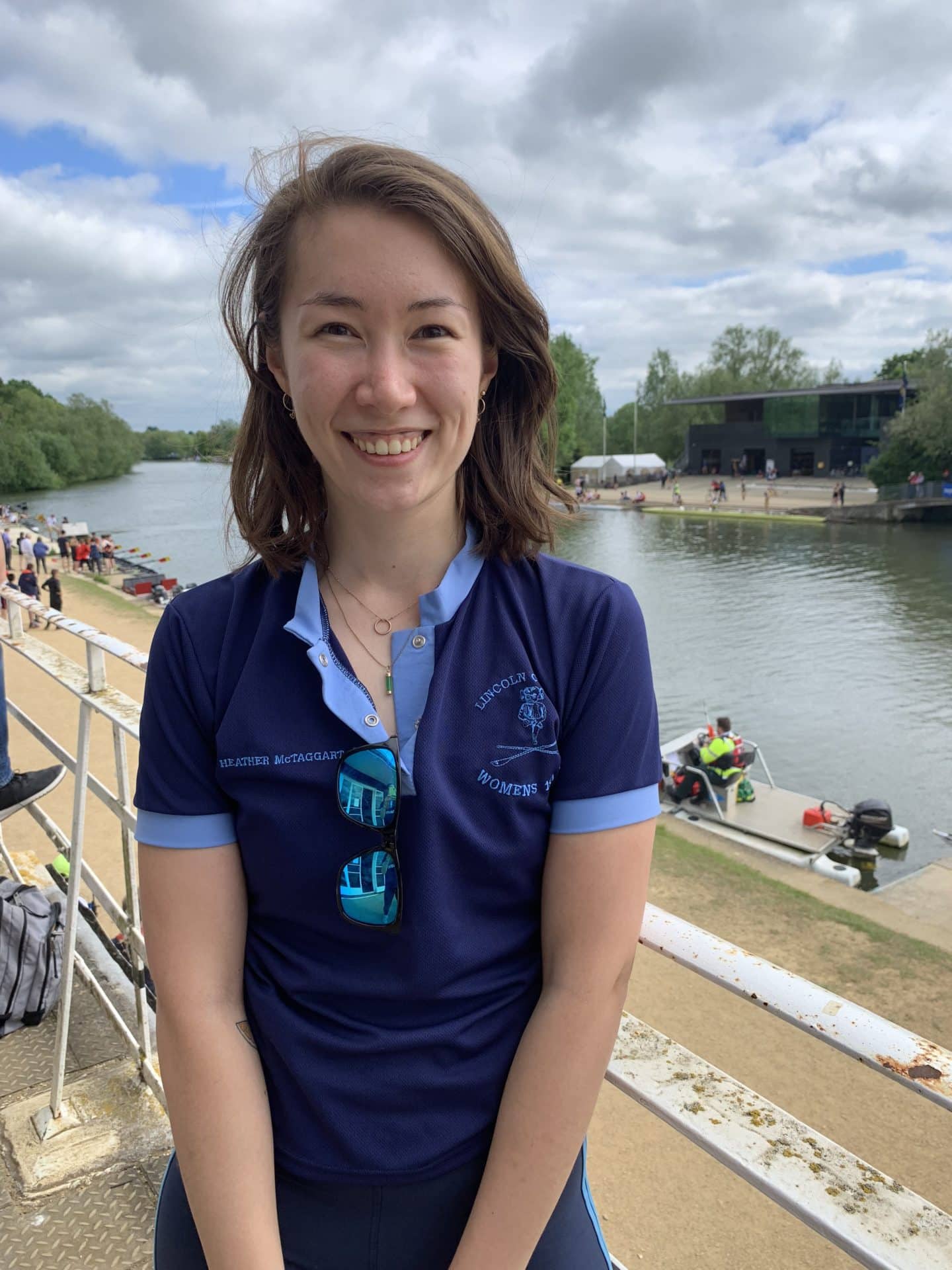 Photograph of Heather McTaggart, a young woman in a blue Lincoln College Women's 1st Boat t-shirt, in front of a river