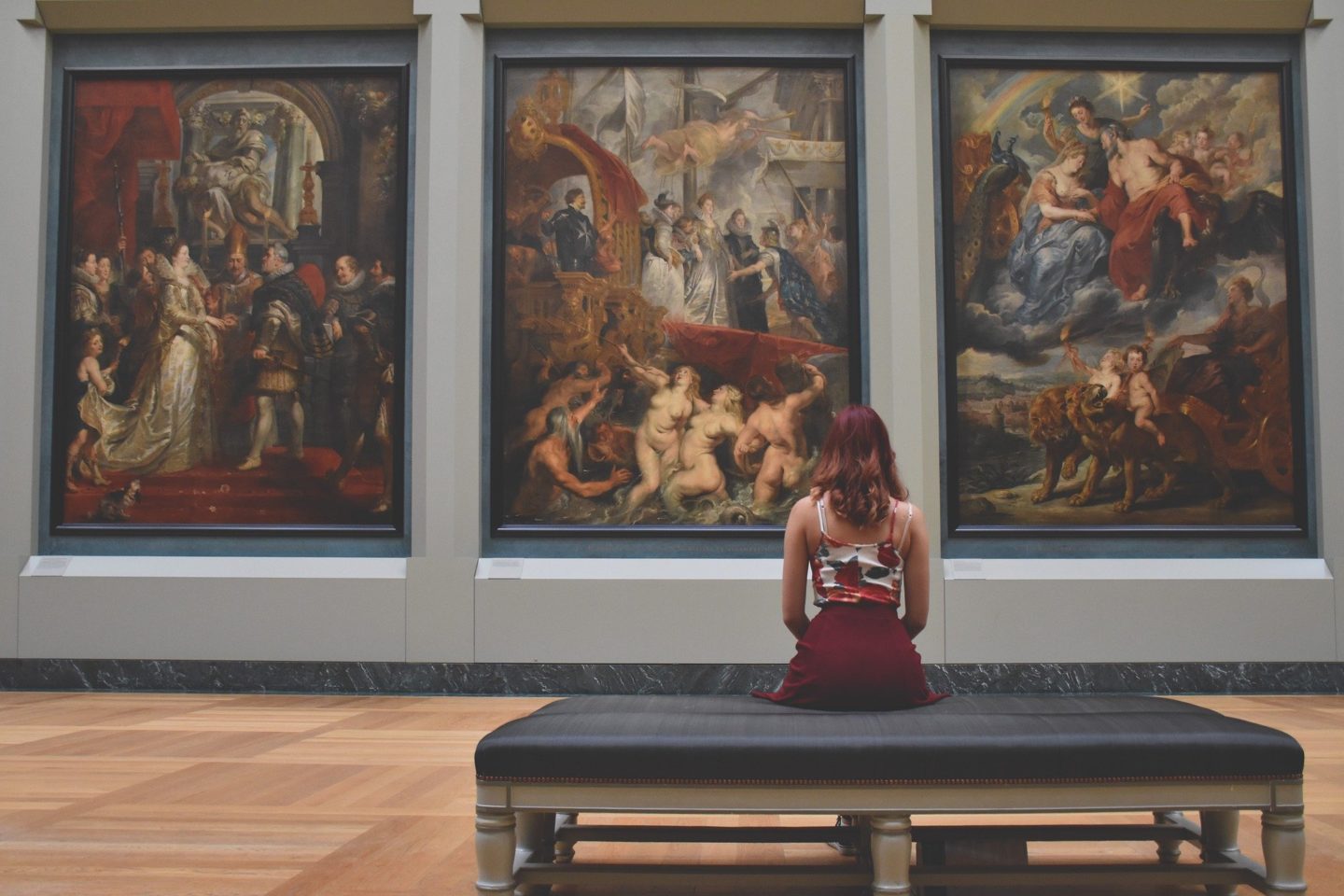 Woman sitting on a bench looking at three large paintings