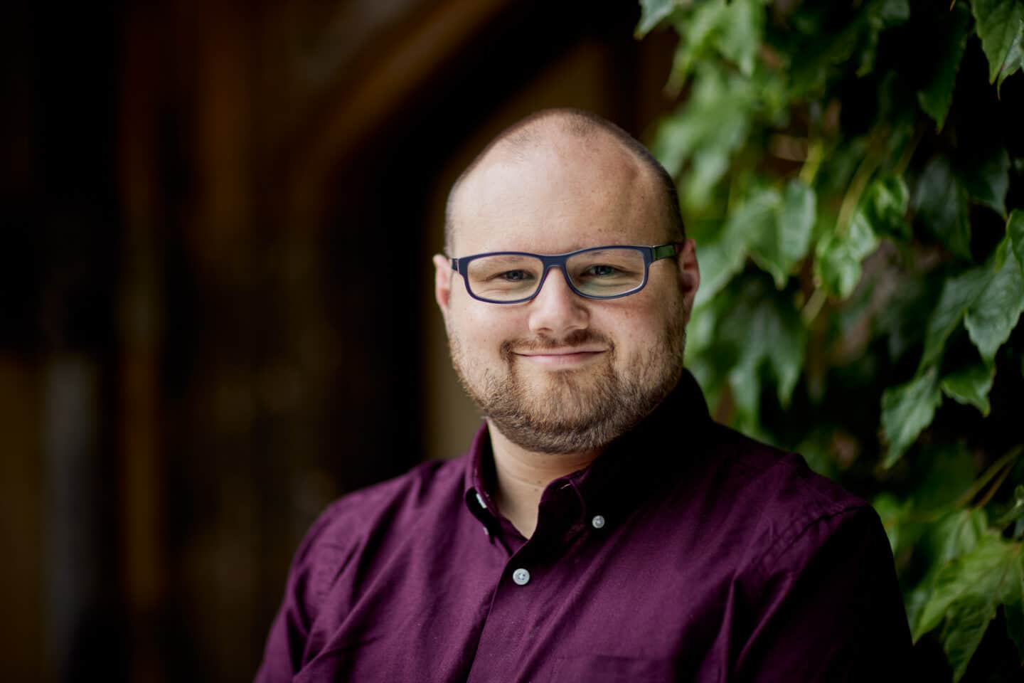 Headshot of Iain Covell, a man in glasses and a purple shirt