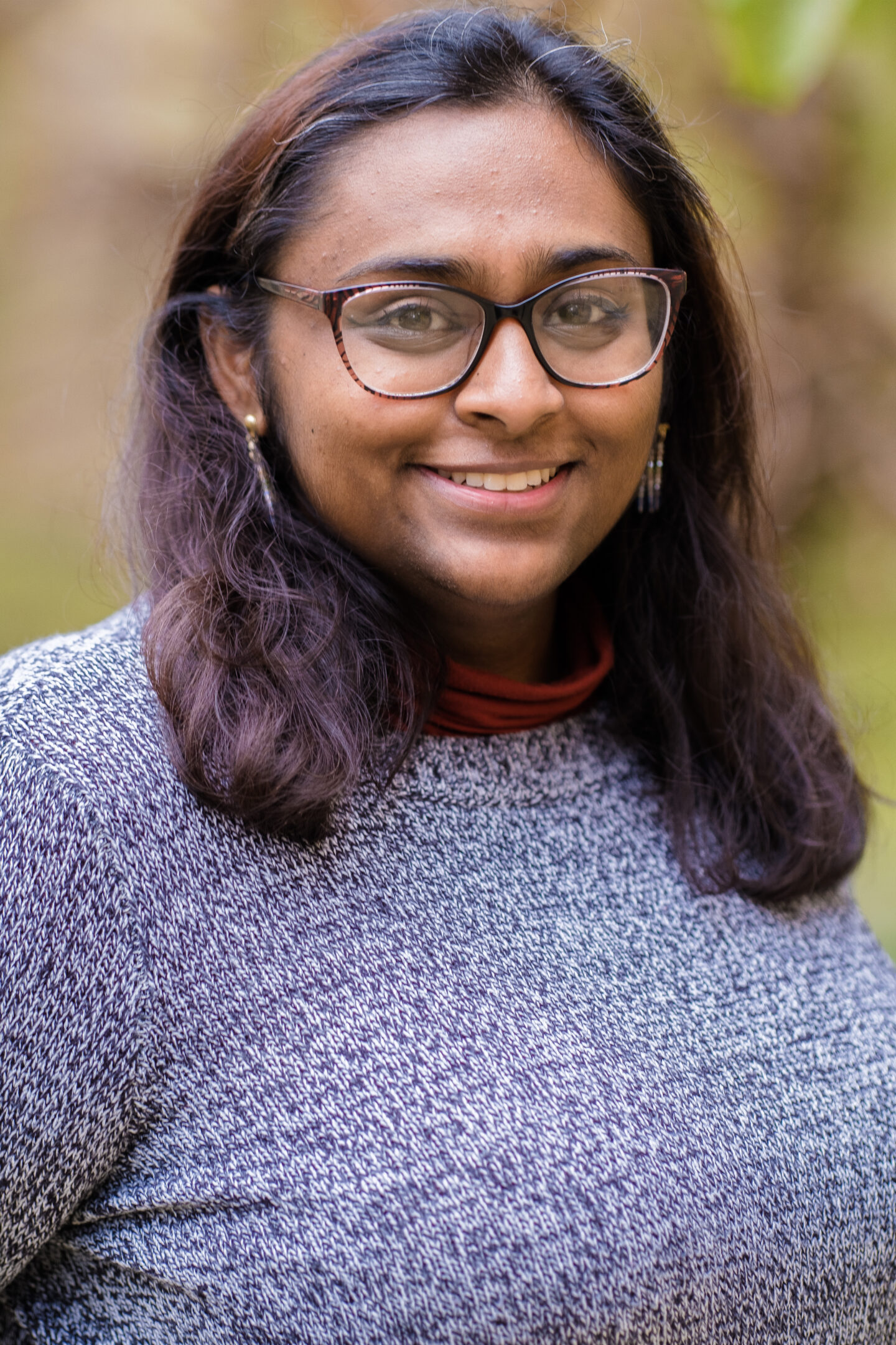 Headshot of Ima Silva, a young woman in glasses and a sweater