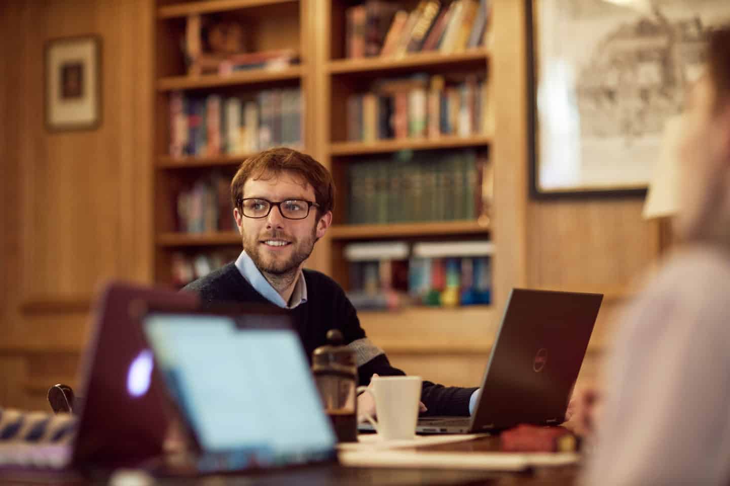 A student sitting with an open laptop and a cup of coffee in the Lincoln College MCR