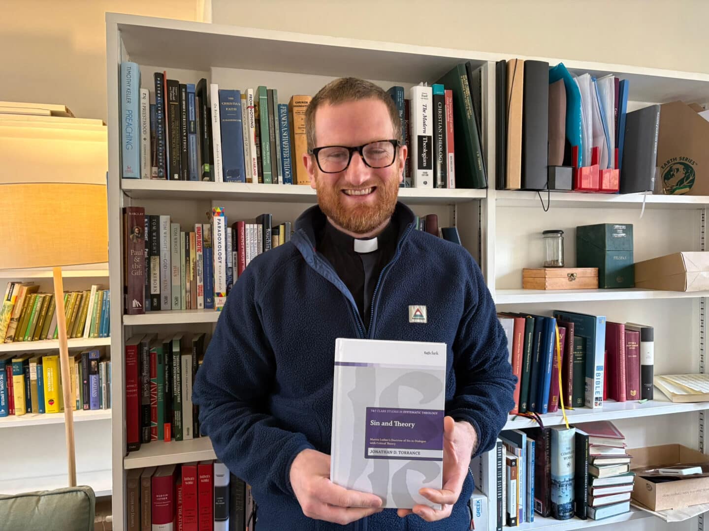 Photo of Jonny Torrance holding his book in his office.
