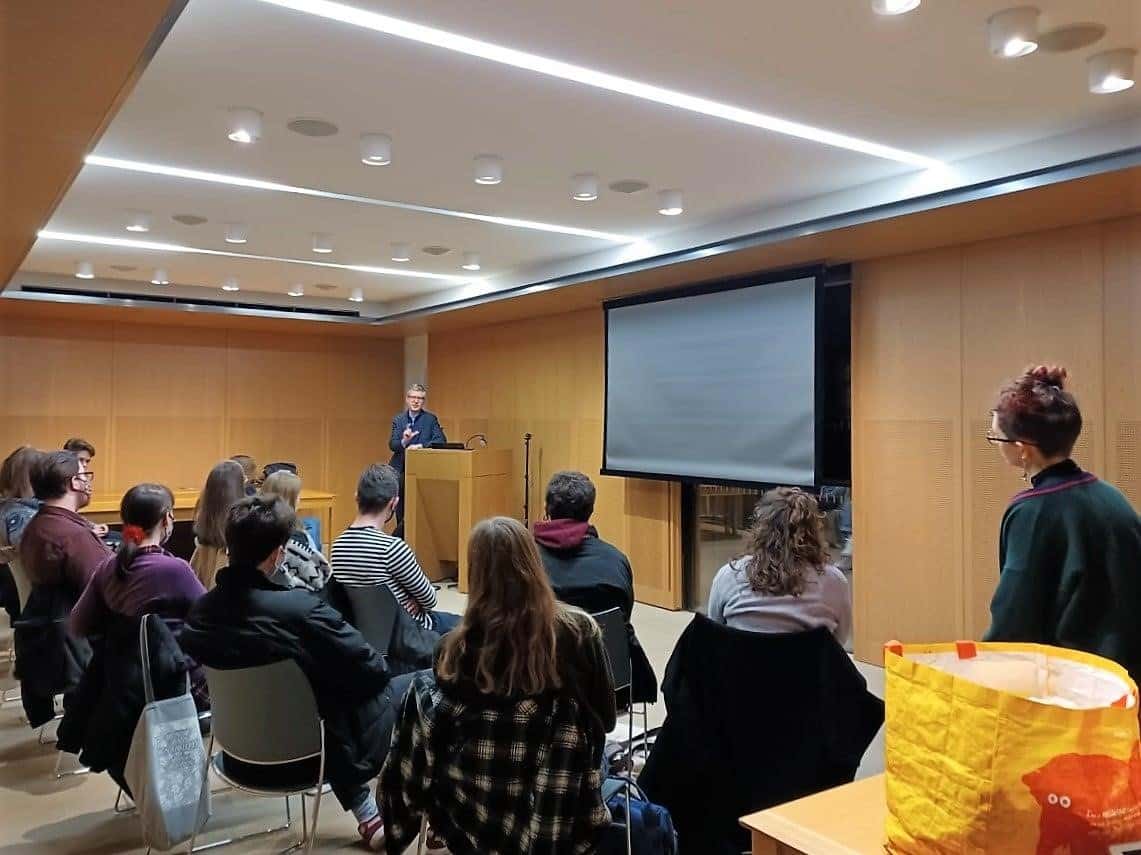 A large group of students sitting in a room watching a male speaker standing at a podium at the front