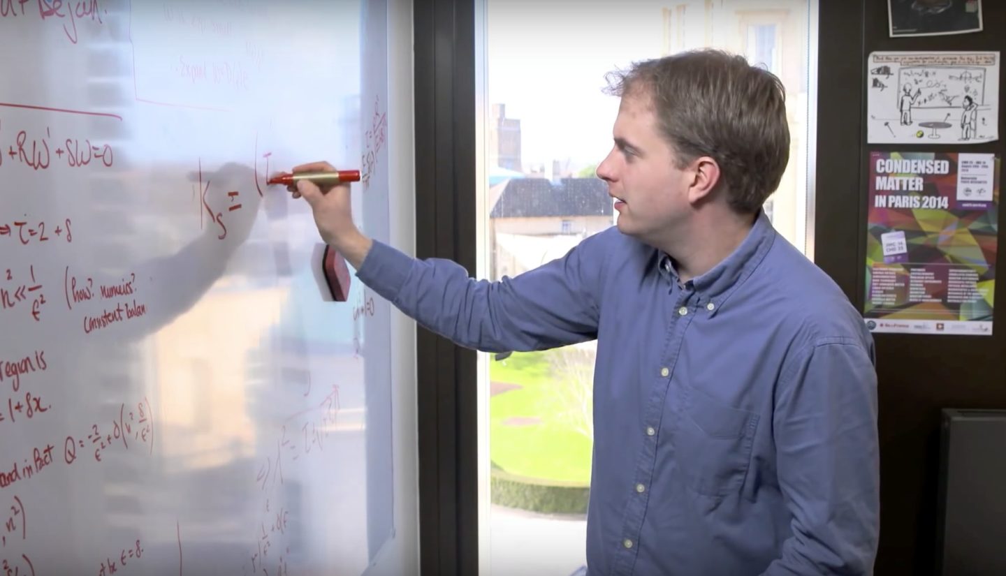 Dominic Vella, a man in a shirt, writing an equation on a whiteboard