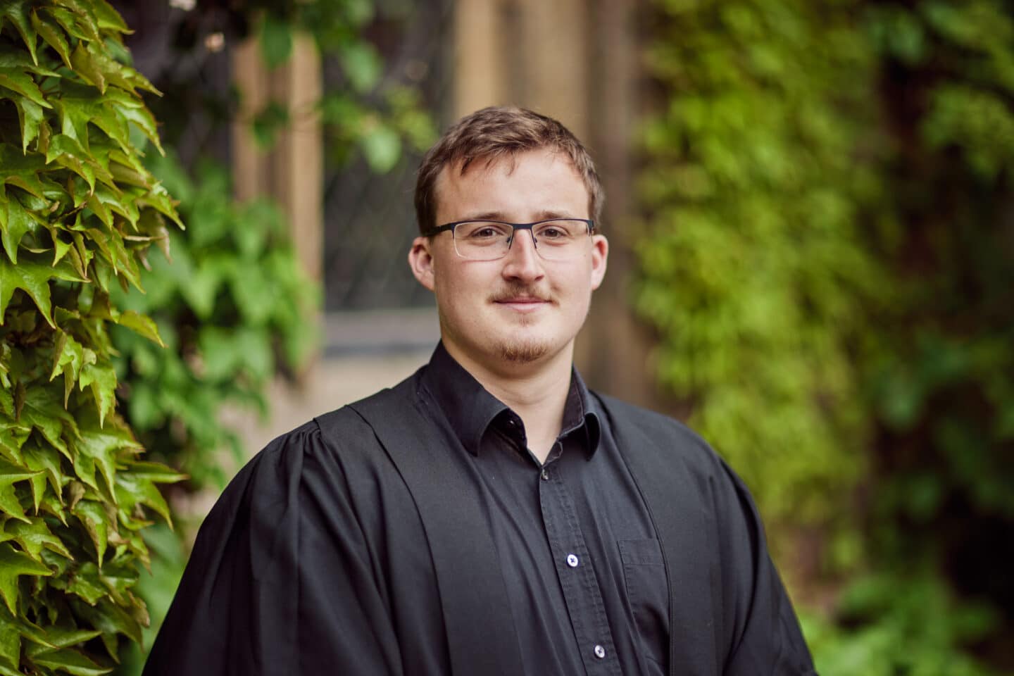 Headshot of Matt Foster, a man in glasses, a black shirt and black robe