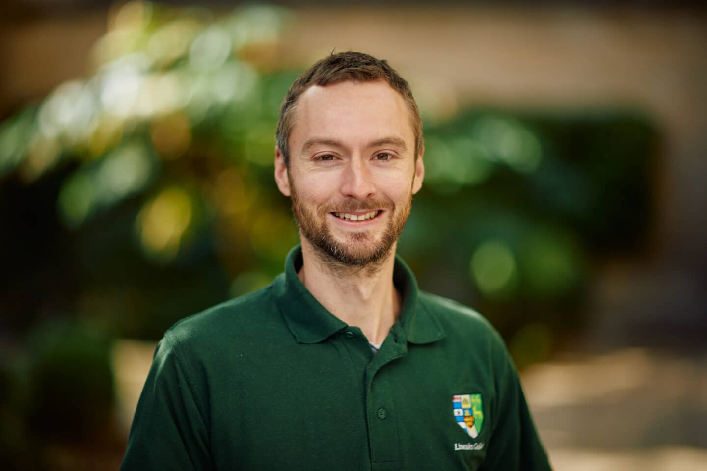 Headshot of the gardener Mike Hawkins, a man wearing a green shirt with the Lincoln College crest.