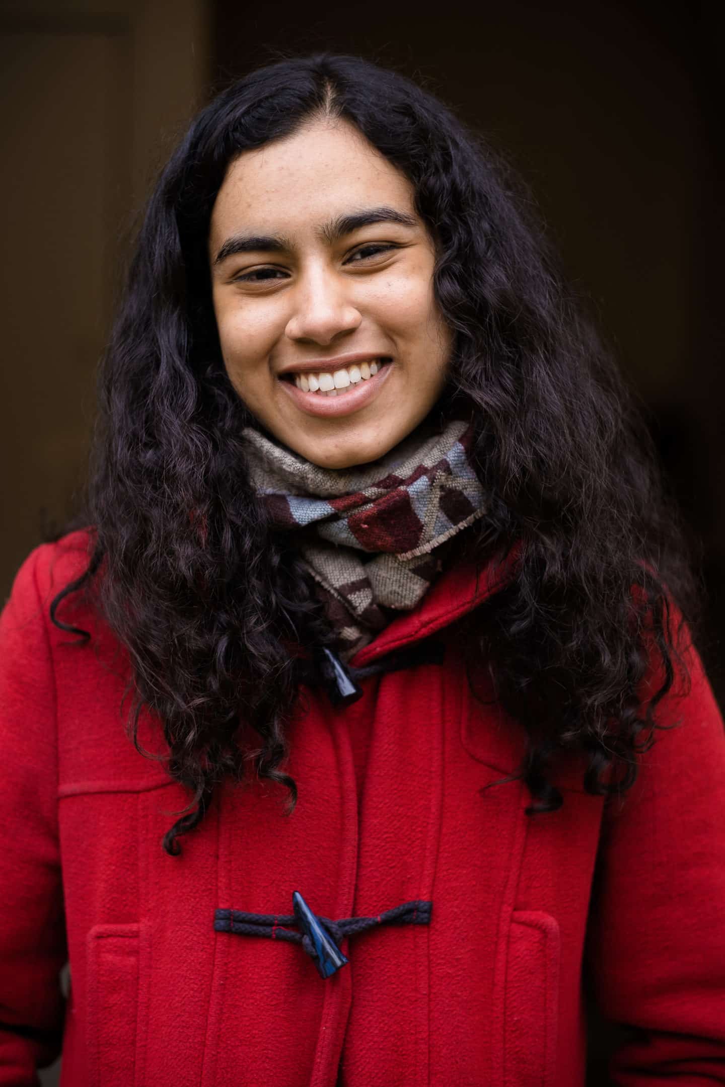 Headshot of Nupur Patel, a young woman in a scarf and red coat