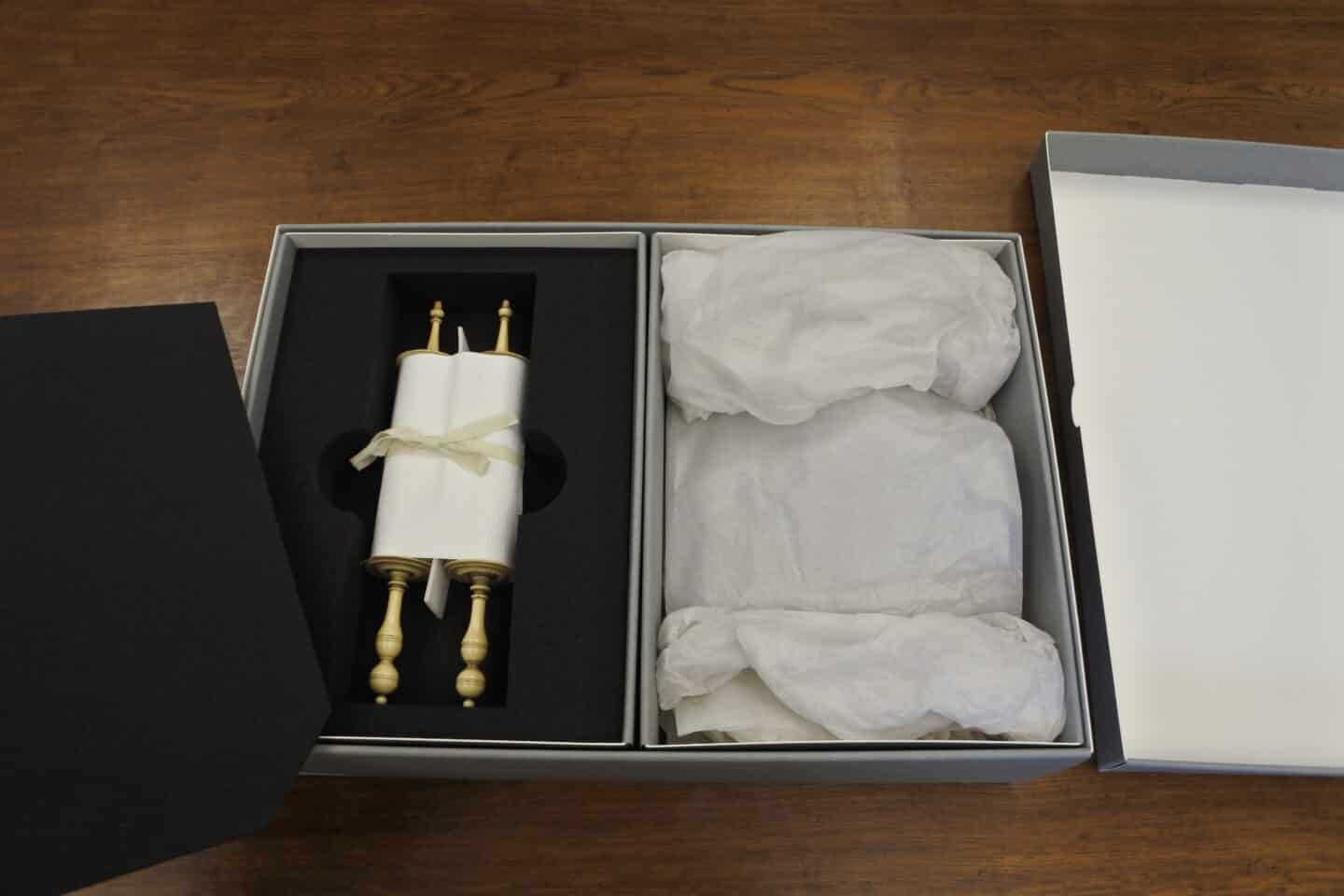 Box containing a safely nested parchment scroll on two ornately turned ivory rollers, bound together by a ribbon