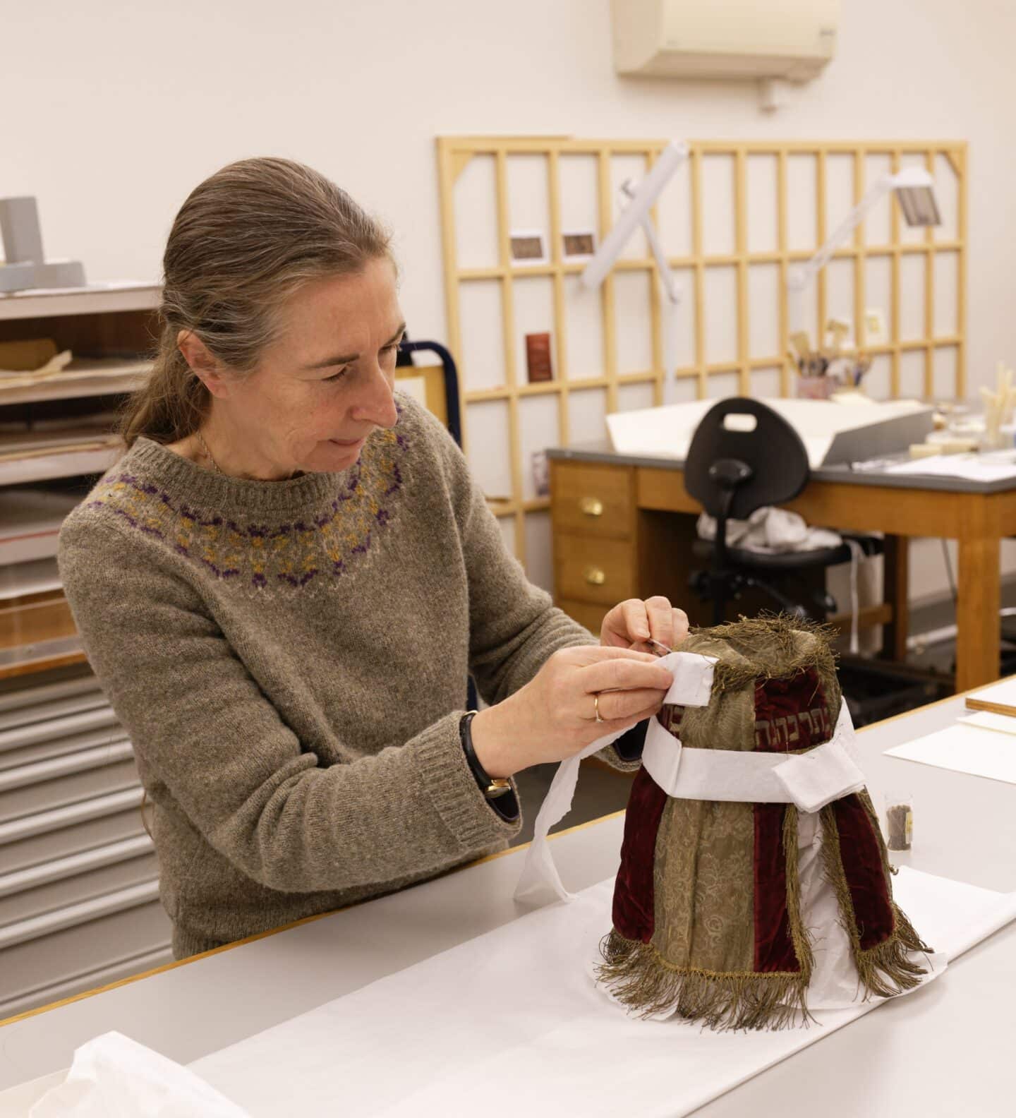 A conservator treating a red and gold mantle by padding it with acid-free tissue