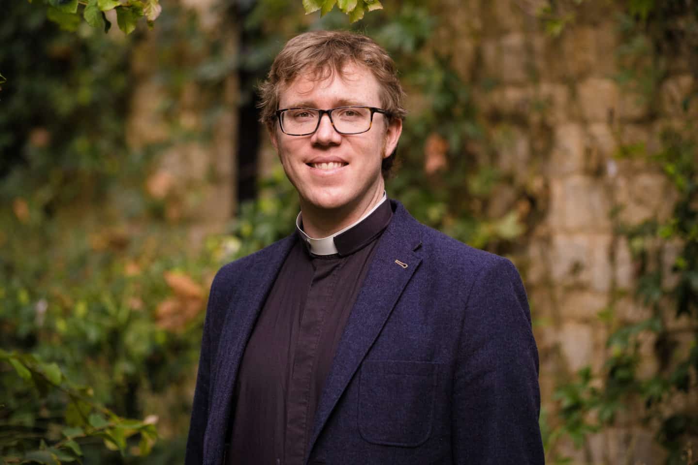 Headshot of the Reverend Andy Shamel, a man wearing a suit with a priest's collar and glasses