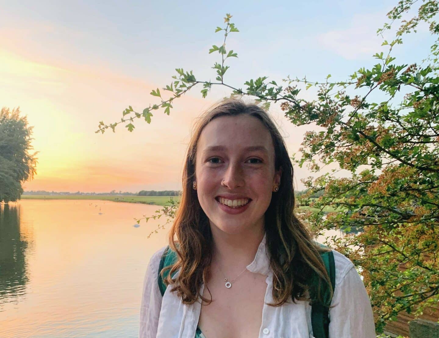 Headshot of Rosie Allwood, a woman in a white top standing in front of a bright lake