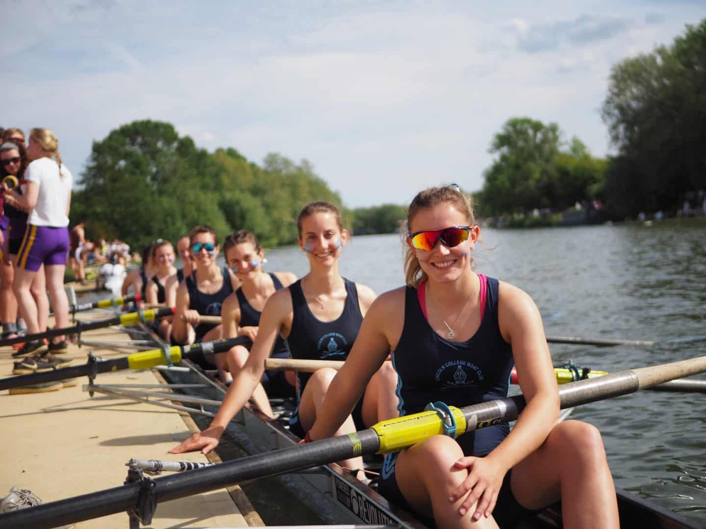 Lincoln College Boat Club Woman's 8, smiling from their boat on the river